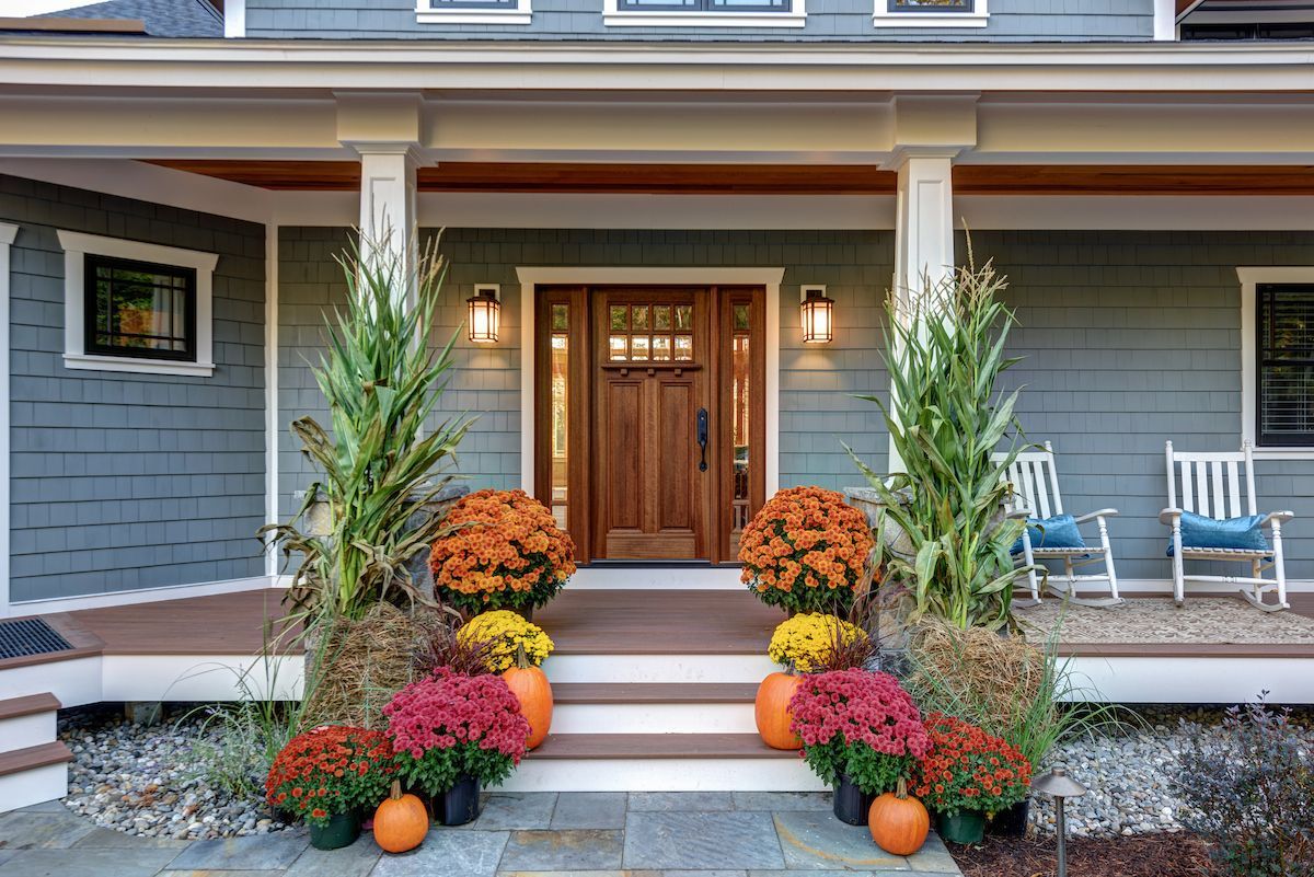 The front porch of a house decorated for fall with pumpkins and flowers.