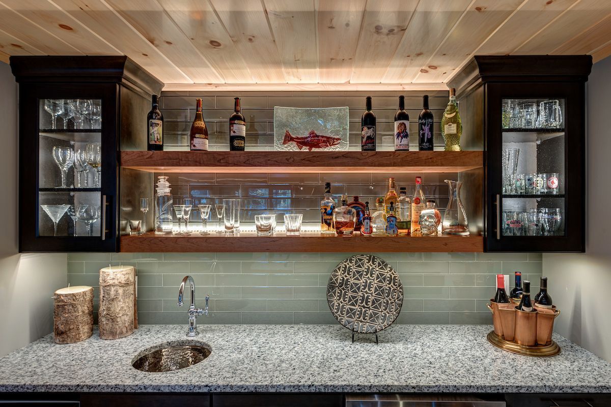 A kitchen with a sink , shelves , bottles and glasses.