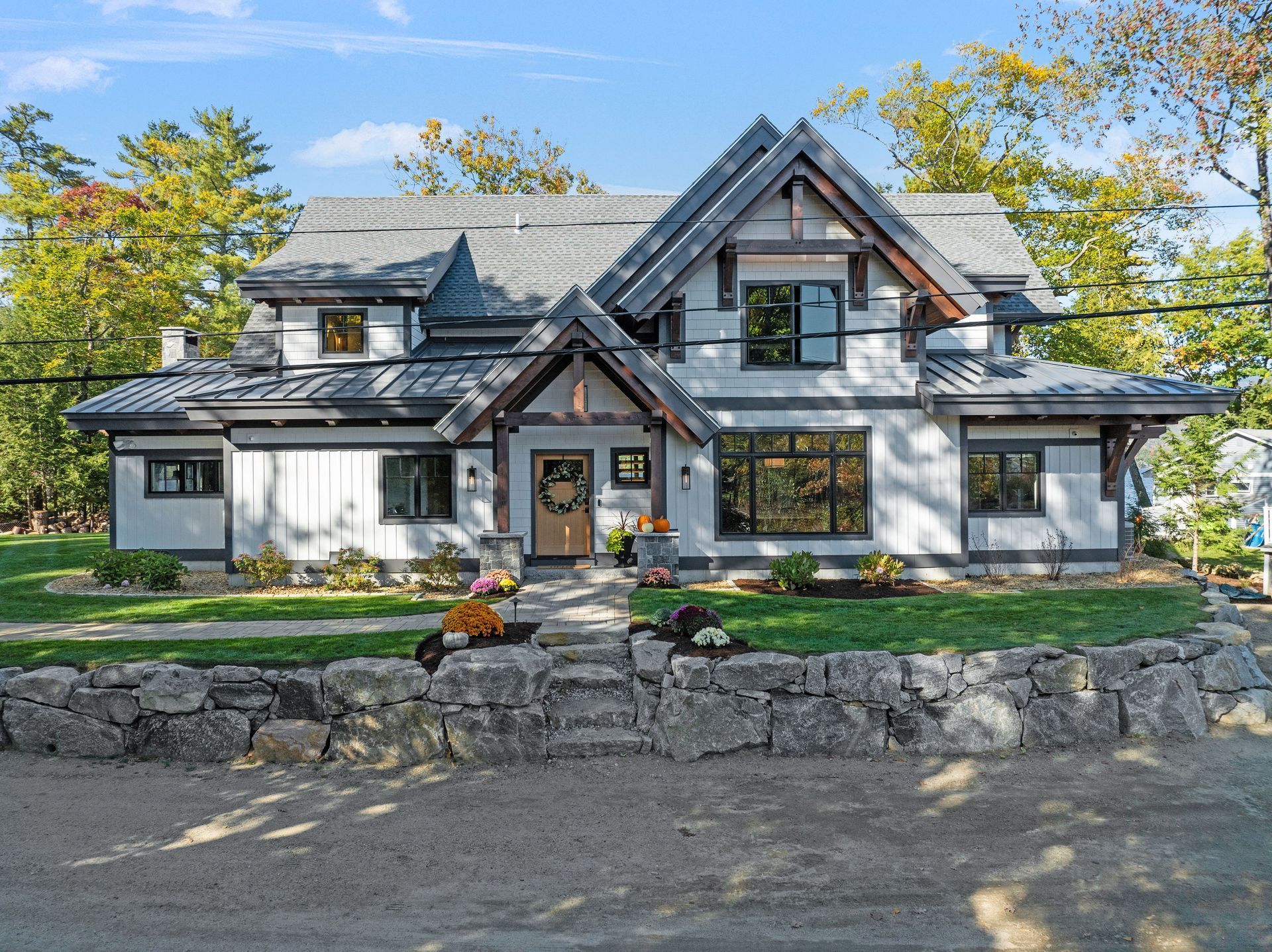 Two-story white house with board-and-batten siding, dark trim, a metal roof, and a stone retaining wall in front.