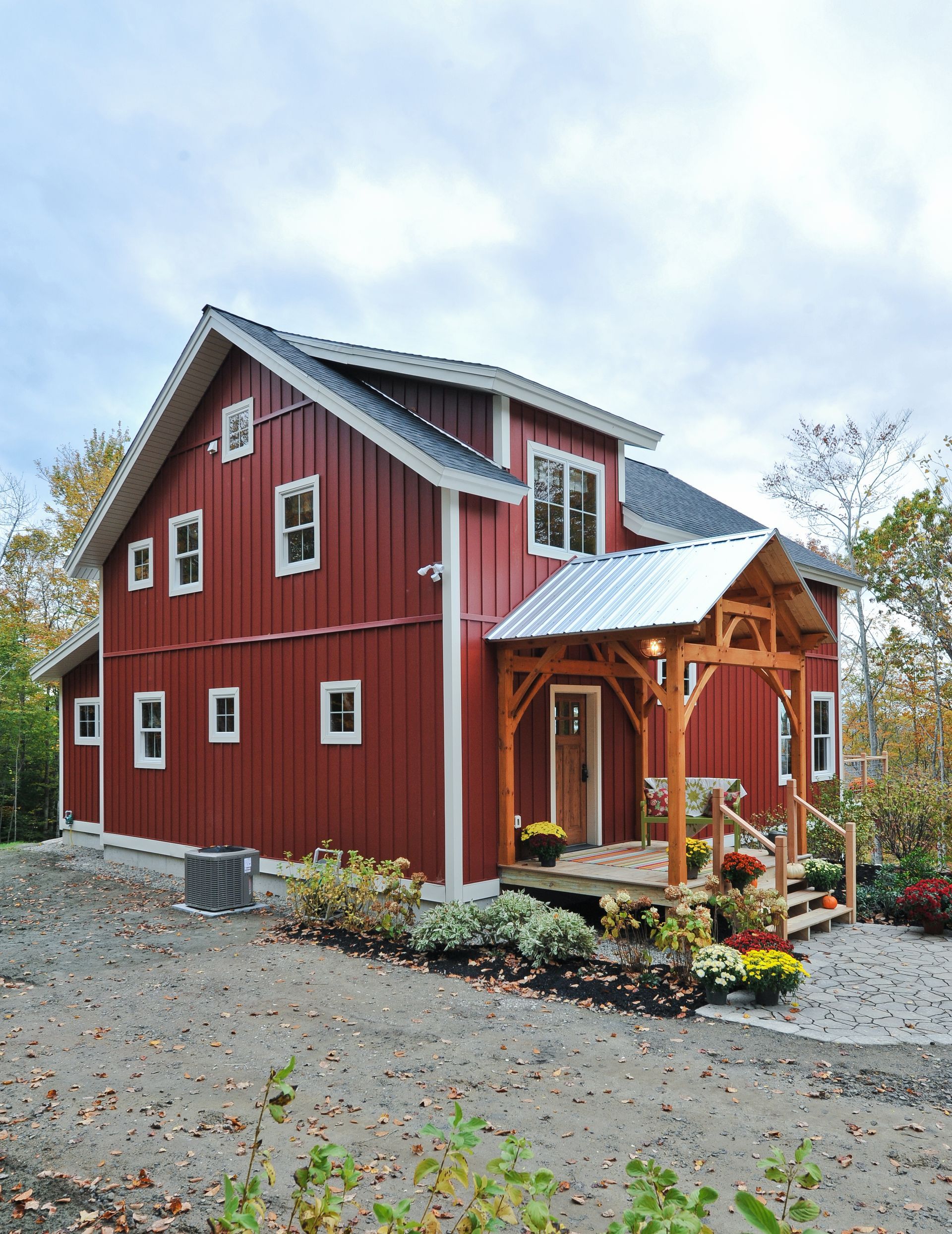 Red two-story house with a porch and gabled roof, set in a gravel yard with vegetation.