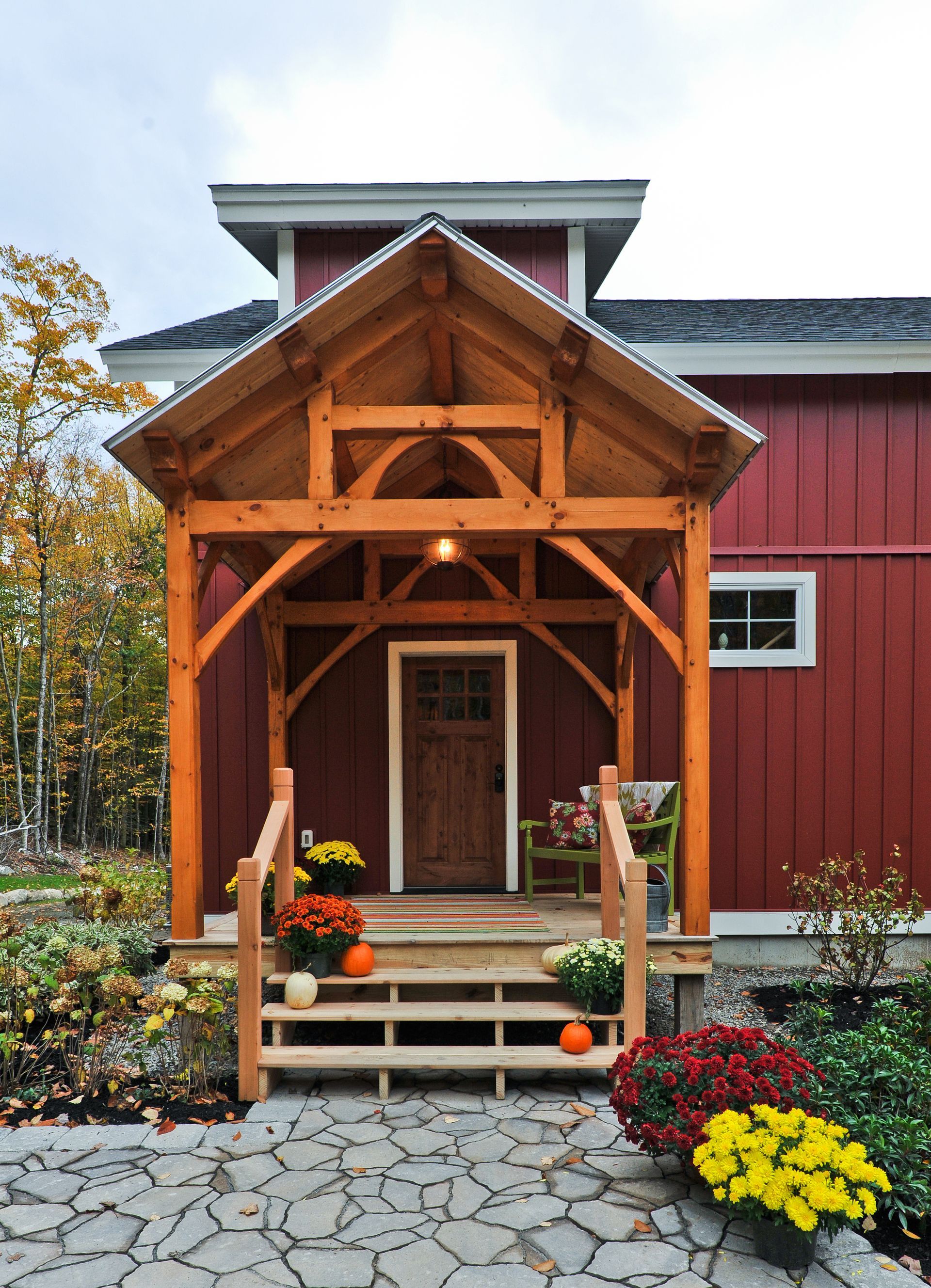 Red barn with wooden porch, stairs, and fall mums; paved stone path.