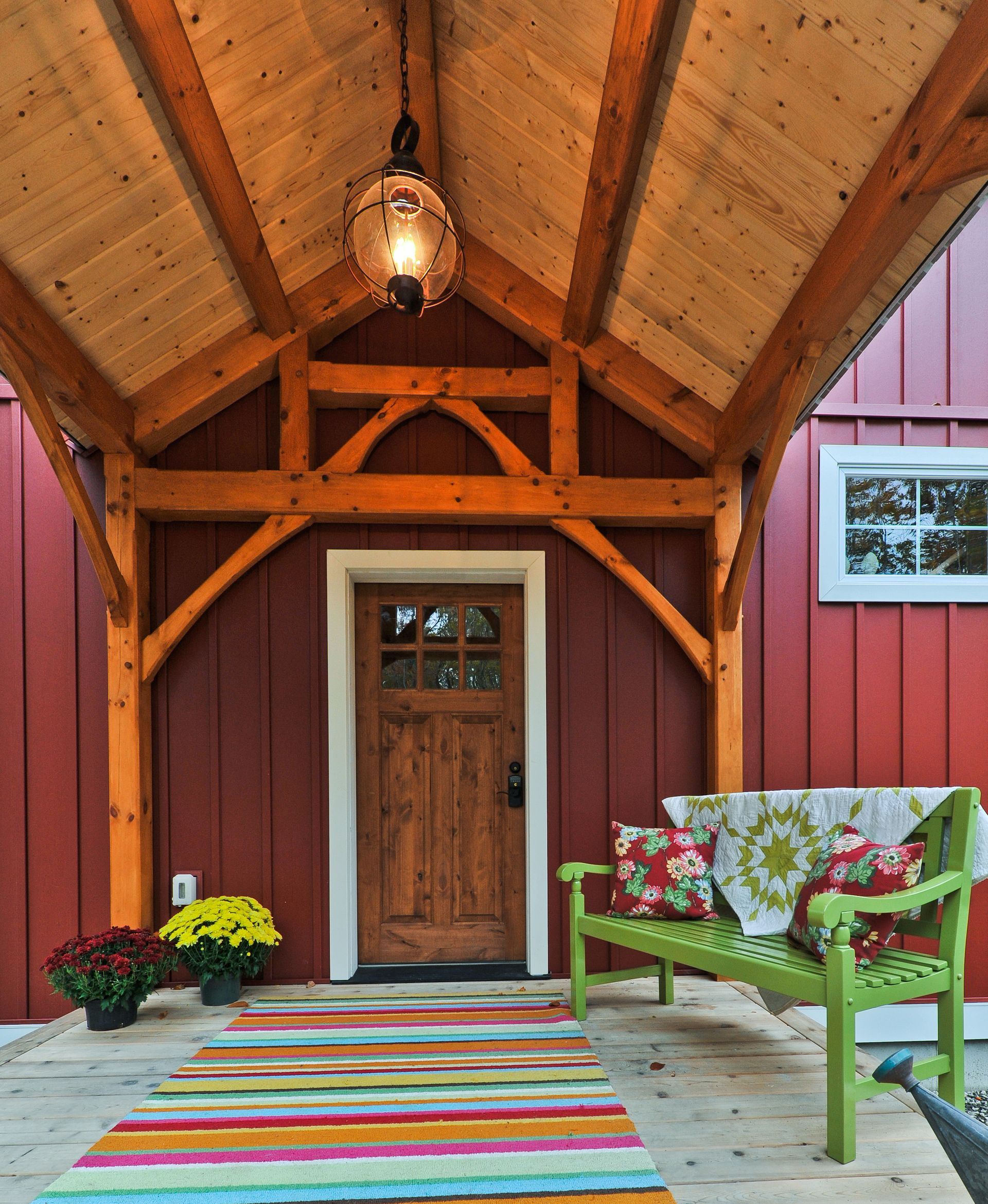 Red house entry with wooden porch, door, and green bench; colorful rug and pillows.