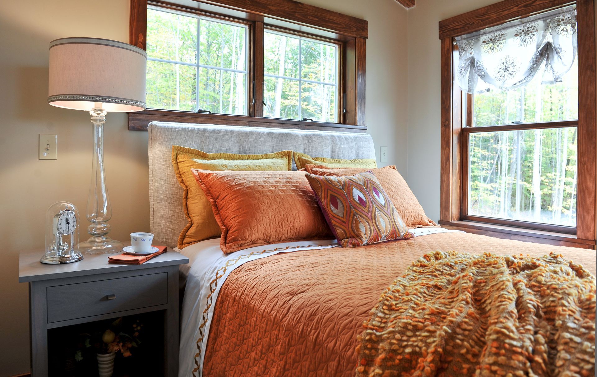 Bedroom with bed featuring orange and yellow bedding, two windows, and a bedside lamp.