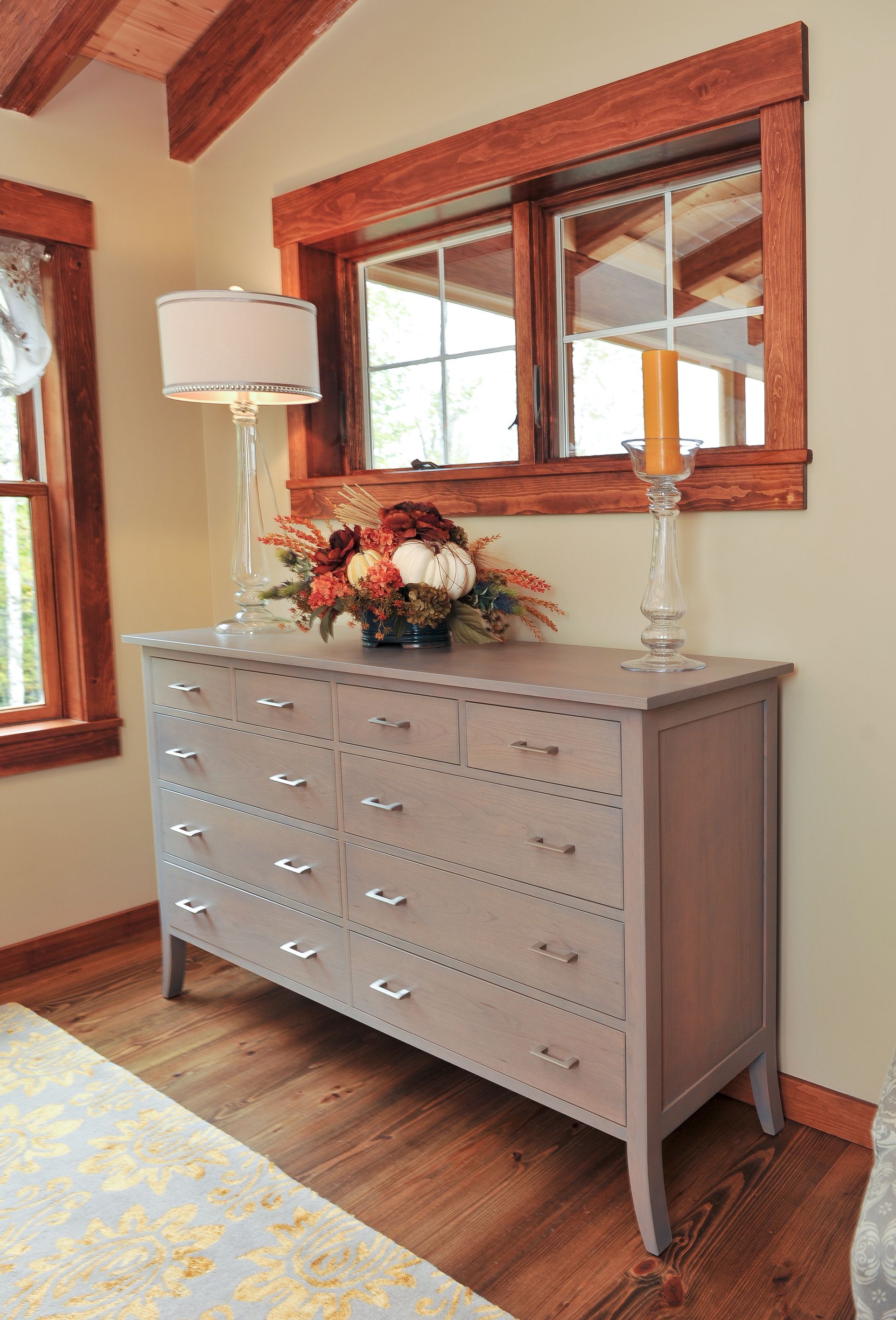 Gray dresser with silver hardware, topped with decor, in a room with a window and hardwood floor.