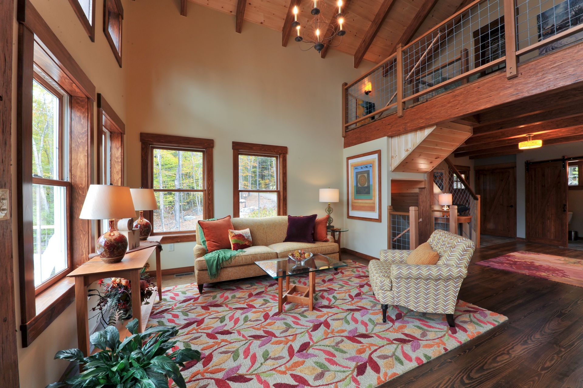 Living room with high ceiling, exposed beams, and a loft. Earth-toned decor, patterned rug, and wooden accents.