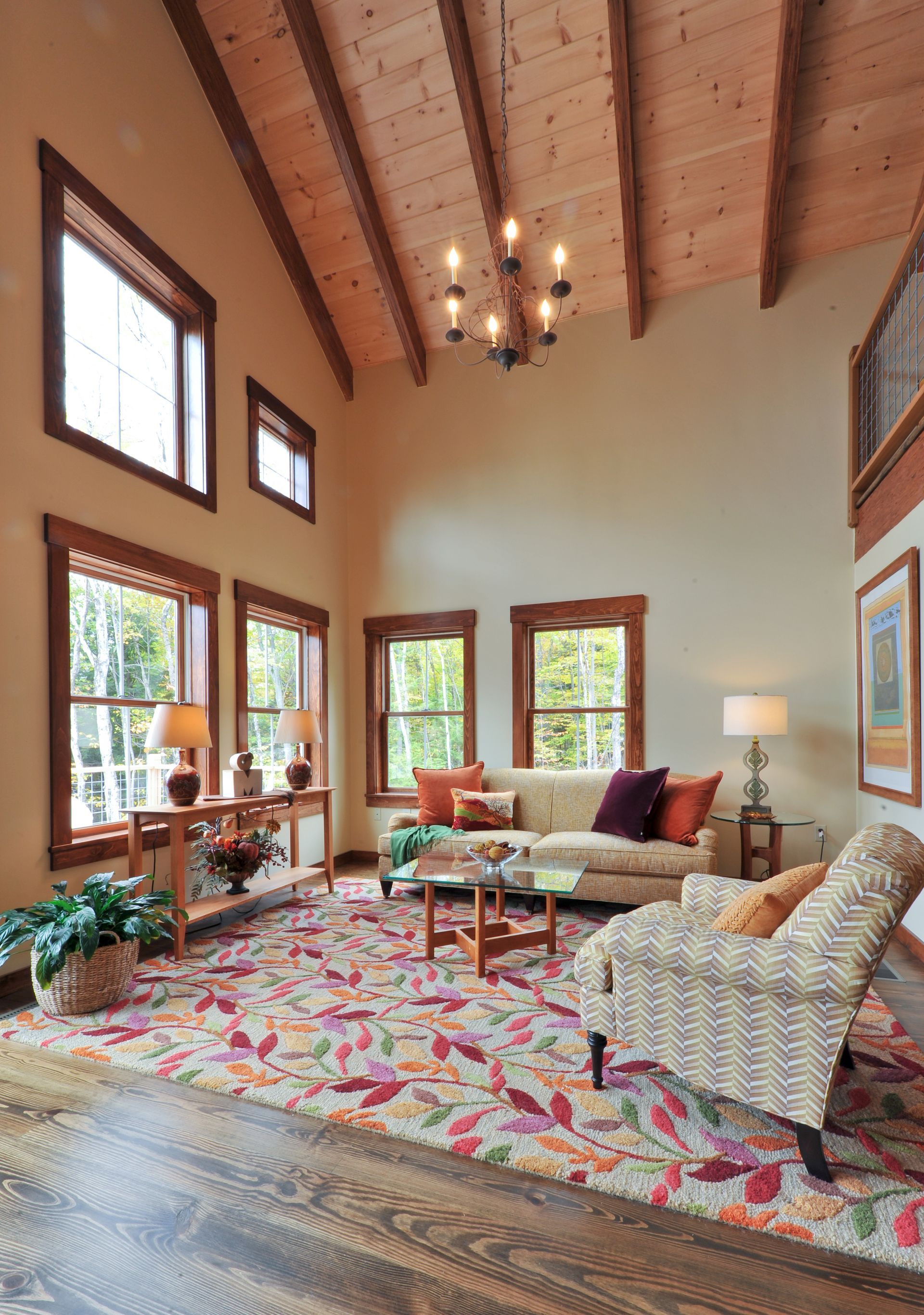 Living room with high ceiling, exposed wooden beams, and colorful floral rug.