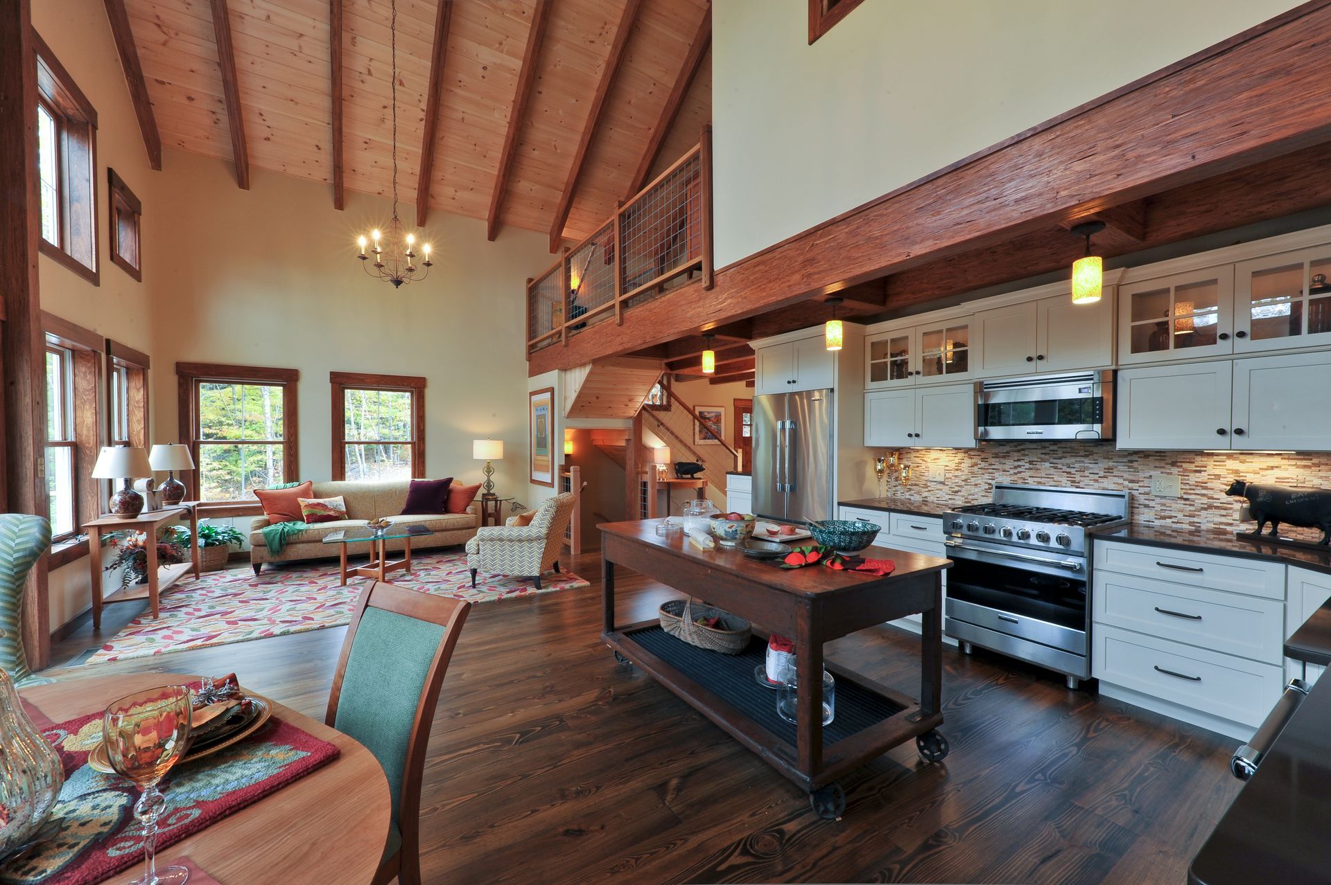 Open-concept kitchen and living area with wood beams, white cabinets, island, and large windows.