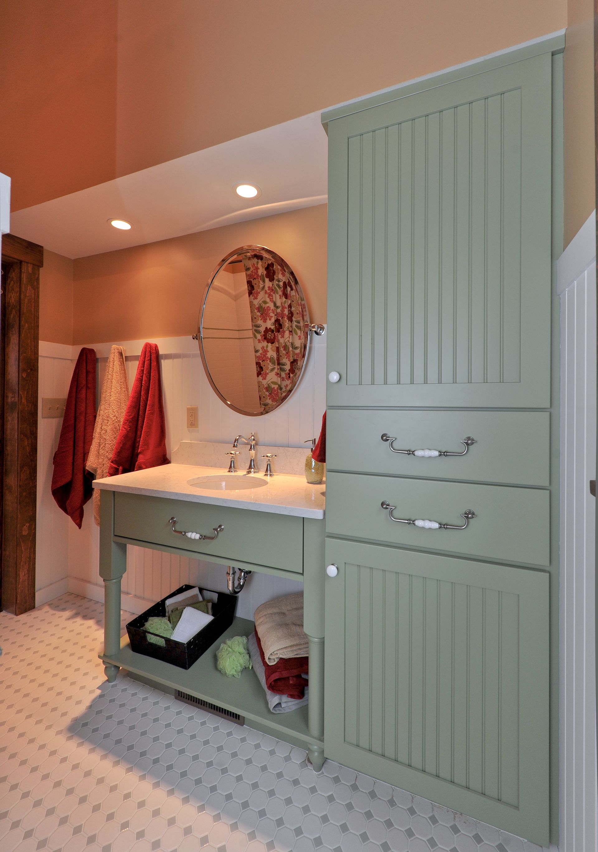 Bathroom with sage green cabinet, white vanity, round mirror, and tile floor.