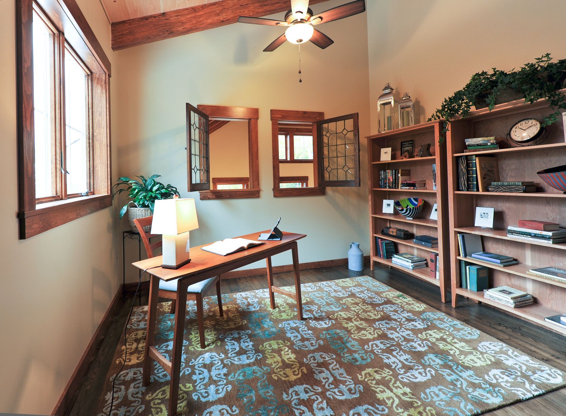 Home office with desk, bookshelves, and rug. Windows let in natural light.