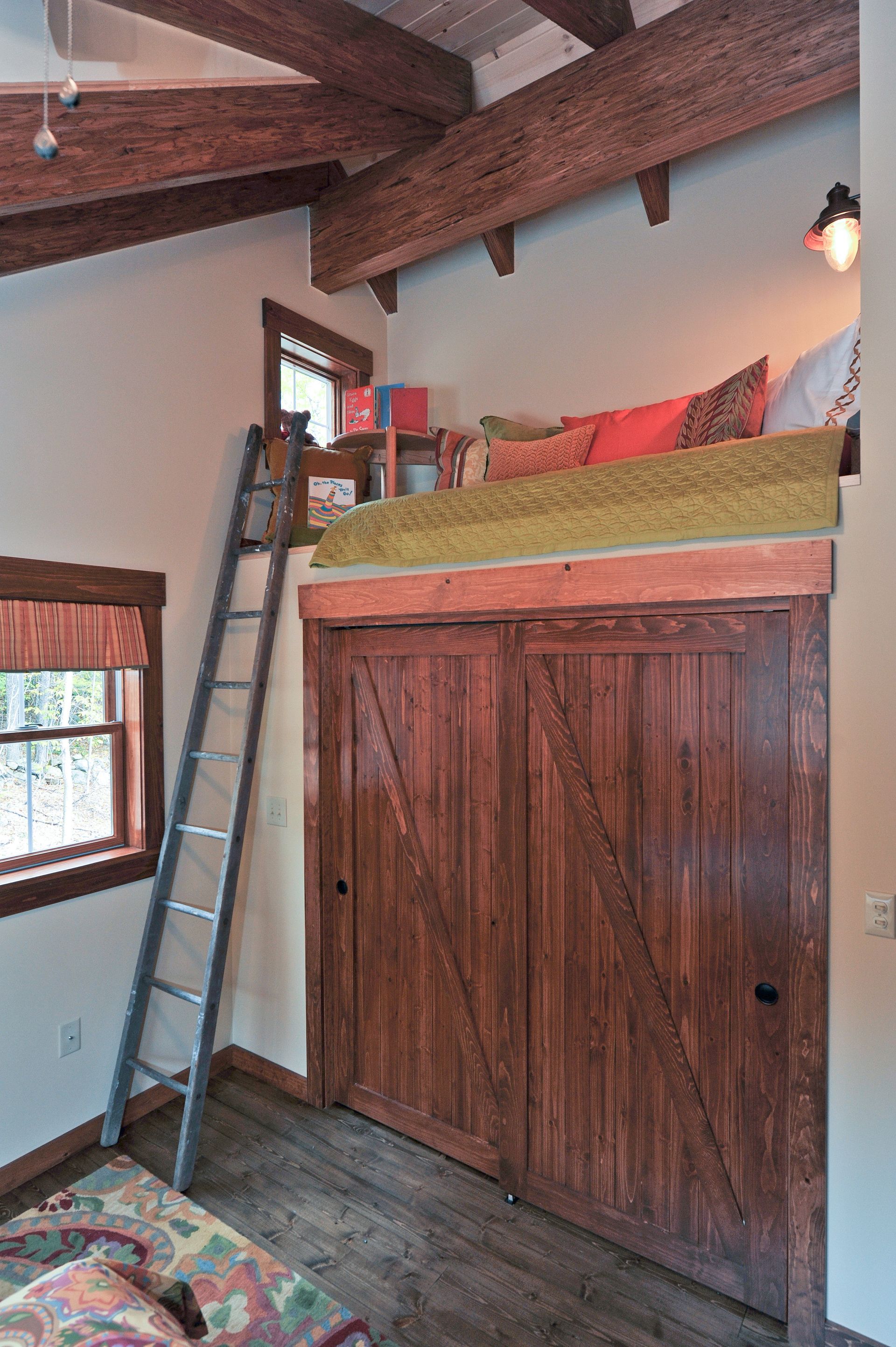 Loft bed over closet, accessed by ladder, rustic wood beams, small window, colorful pillows.