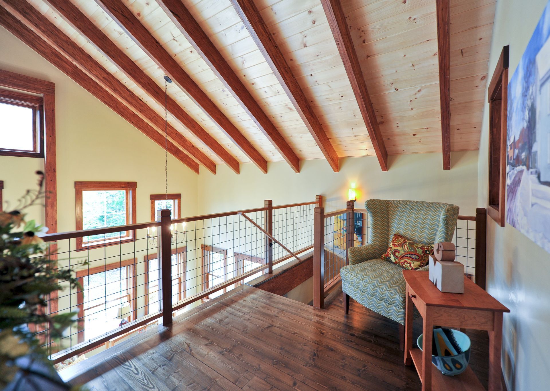 Loft with exposed wooden beams, railing, chair, and side table. Warm tones, natural light.