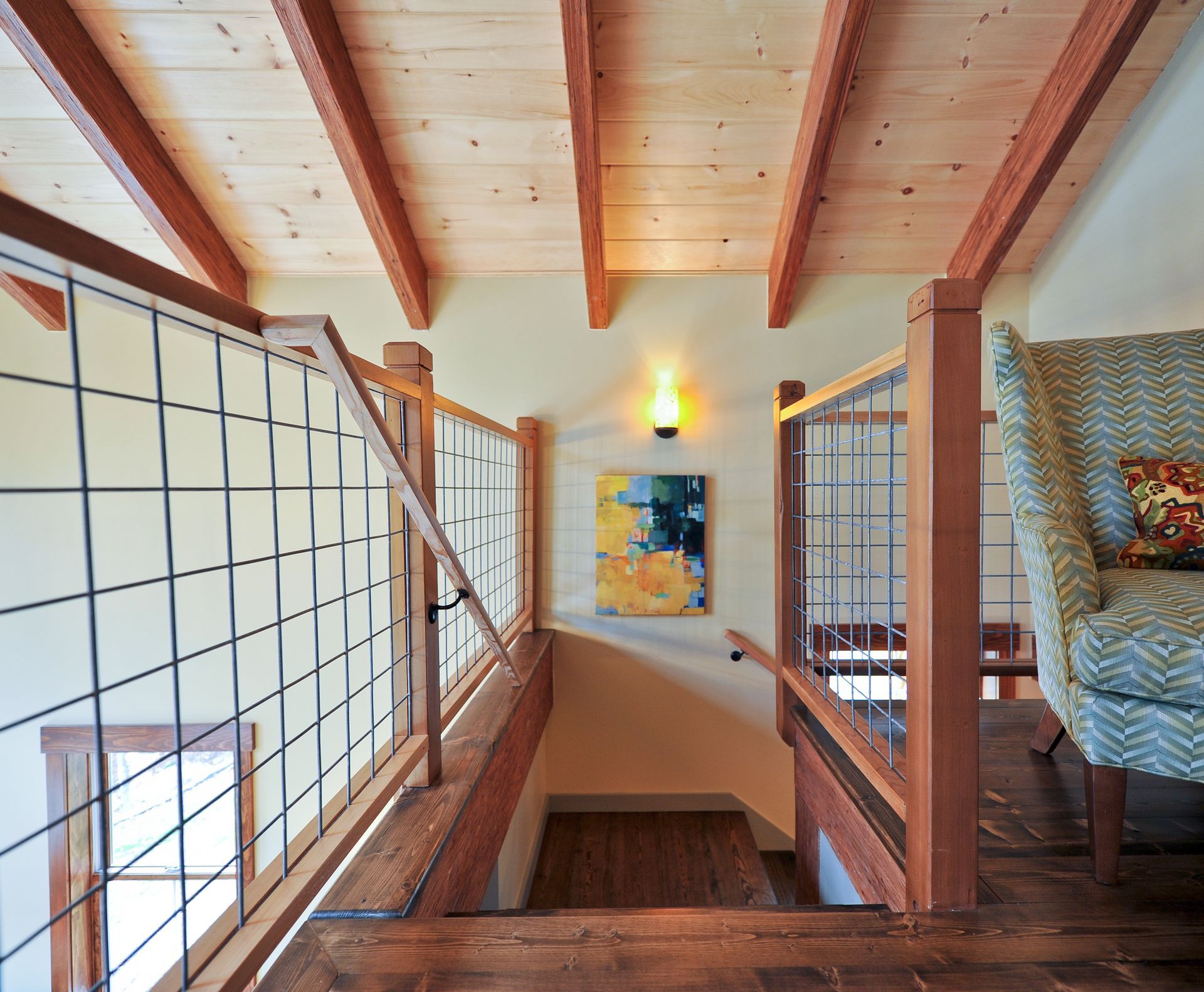 Wooden staircase with wire railings, leading down.  Beams overhead, chair in the corner.
