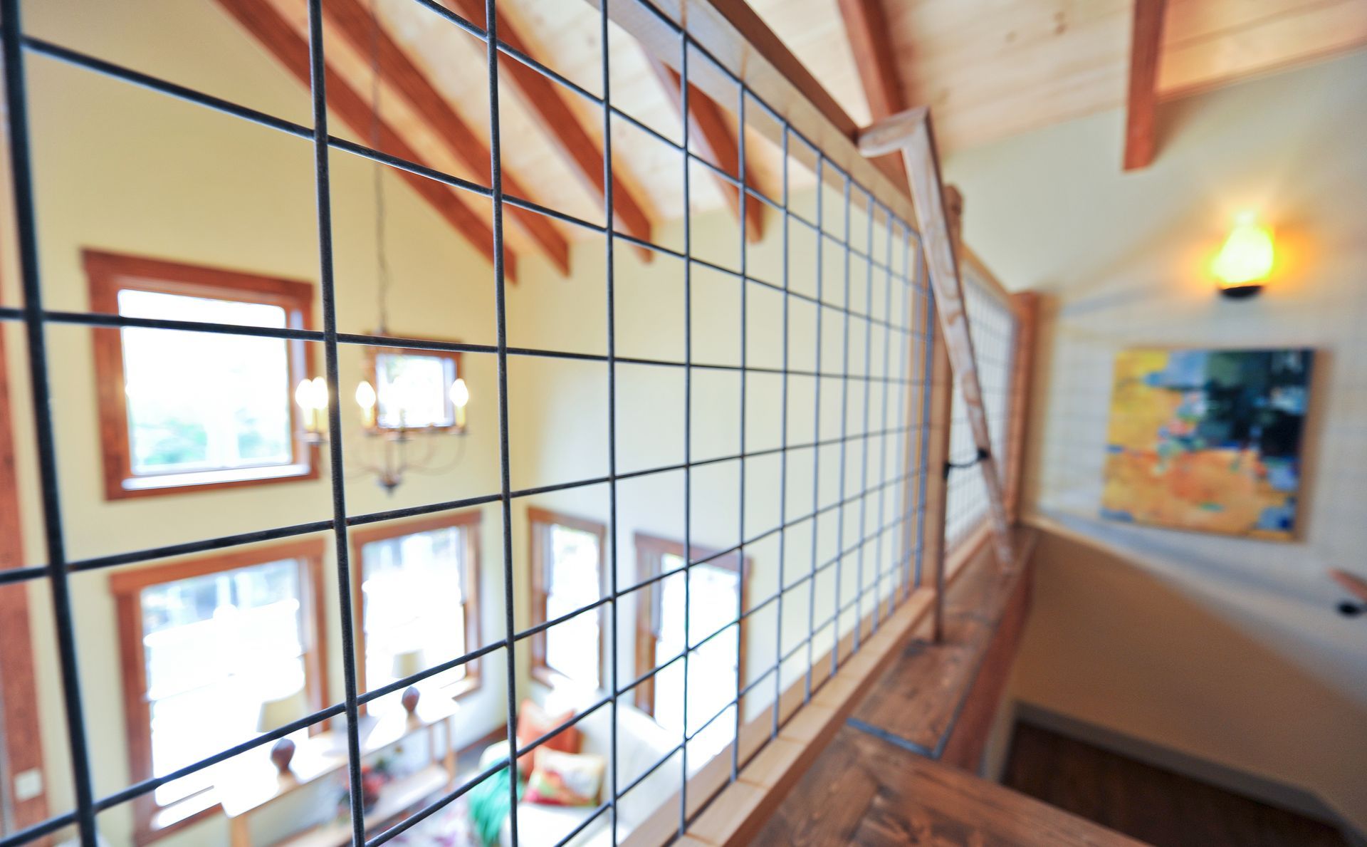 Interior view of a loft with a metal mesh railing, looking down at the living area with windows and artwork.