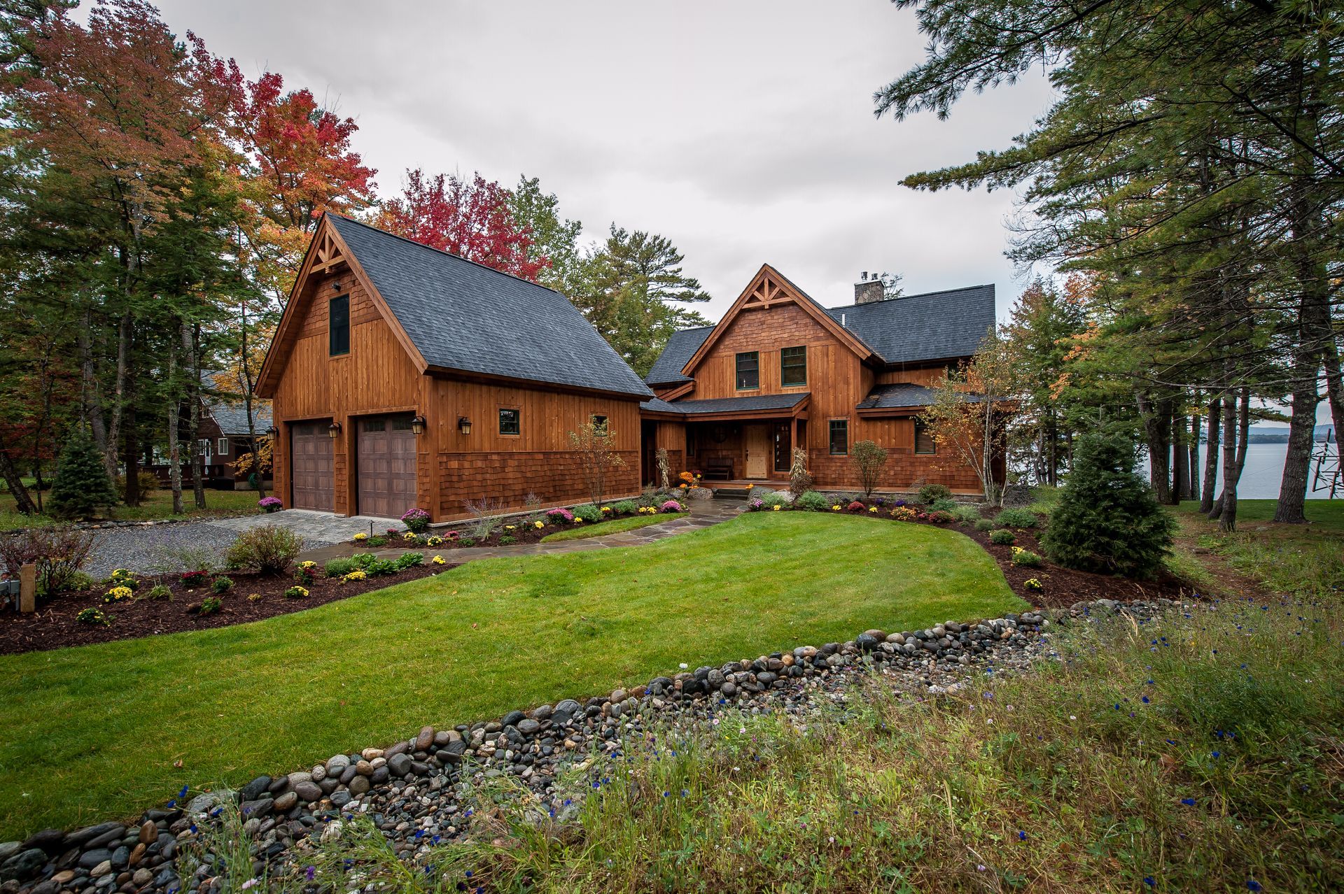 Wood-clad house with a matching garage, lawn, and colorful fall trees on a lakeside property.