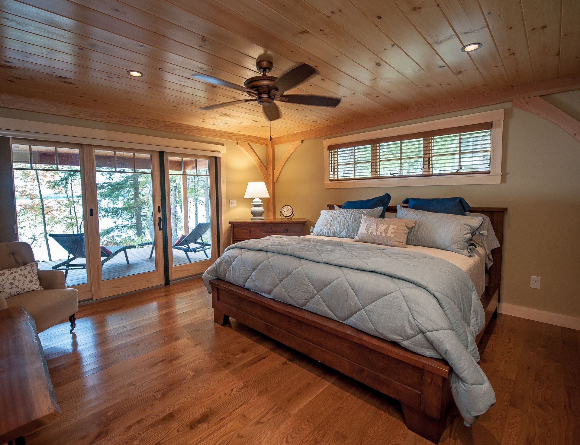 Bedroom with wooden floors and ceiling, large bed, sliding door to deck, and lake view.