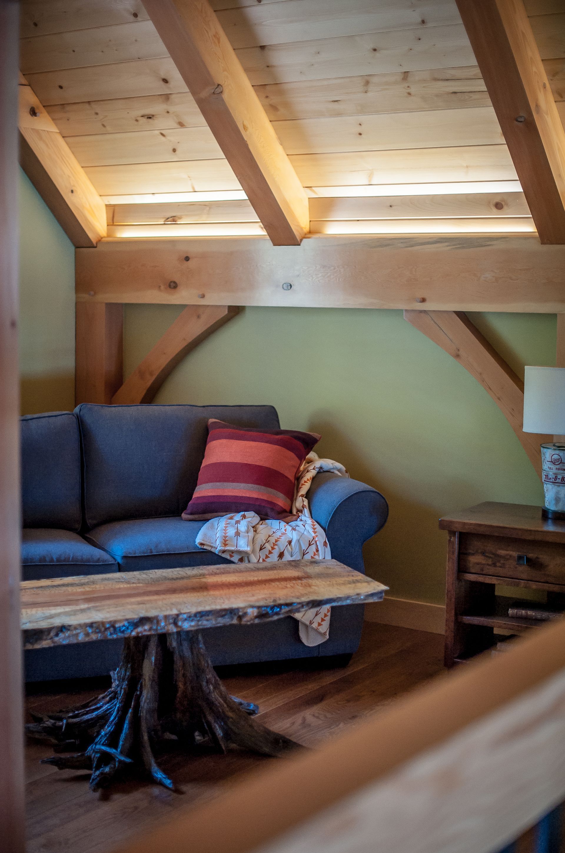 Cozy living area with wooden beams, gray couch, live-edge coffee table, and rustic side table.