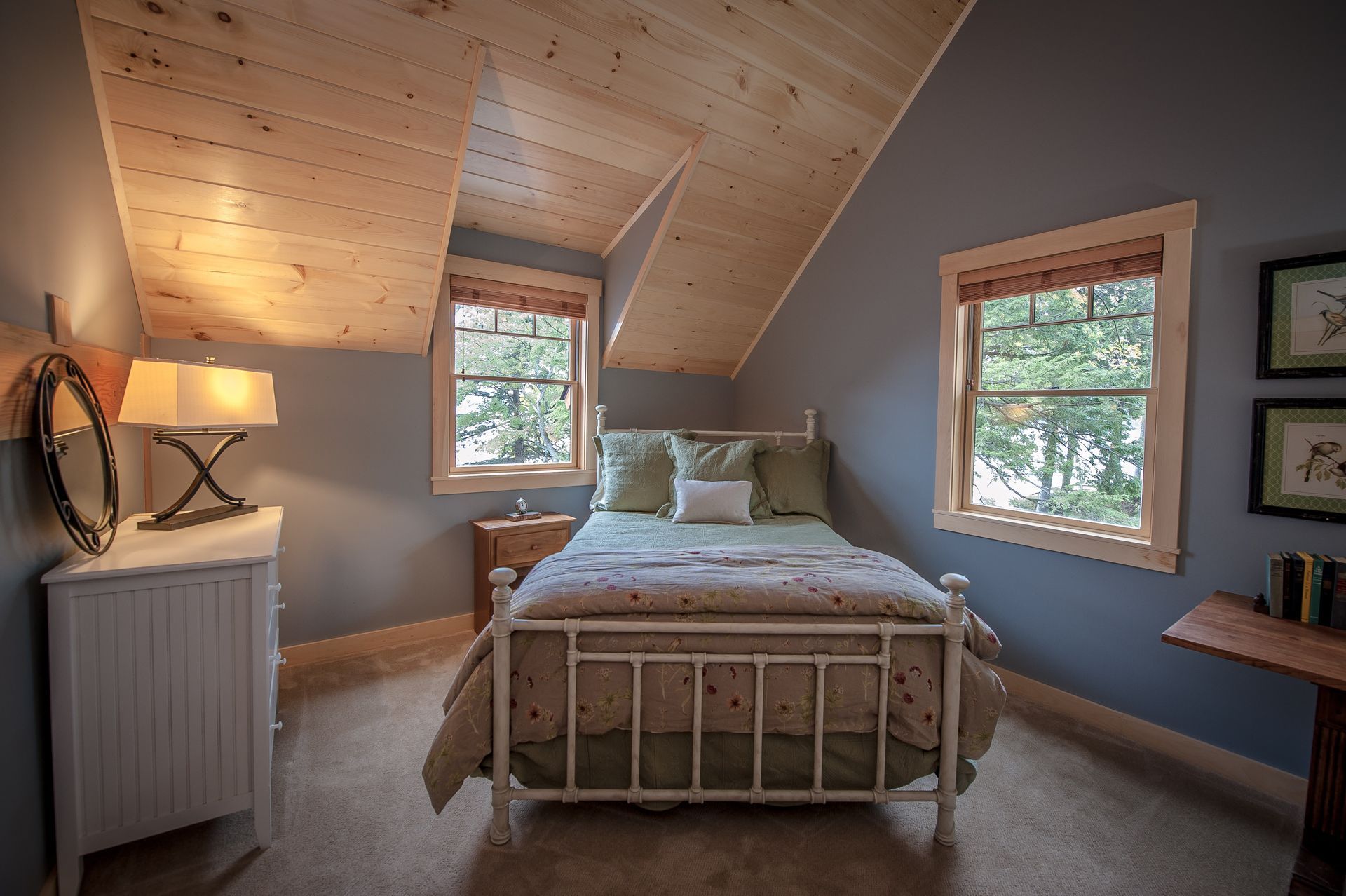 Bedroom with light wood ceiling, blue walls, metal bed frame, and two windows.