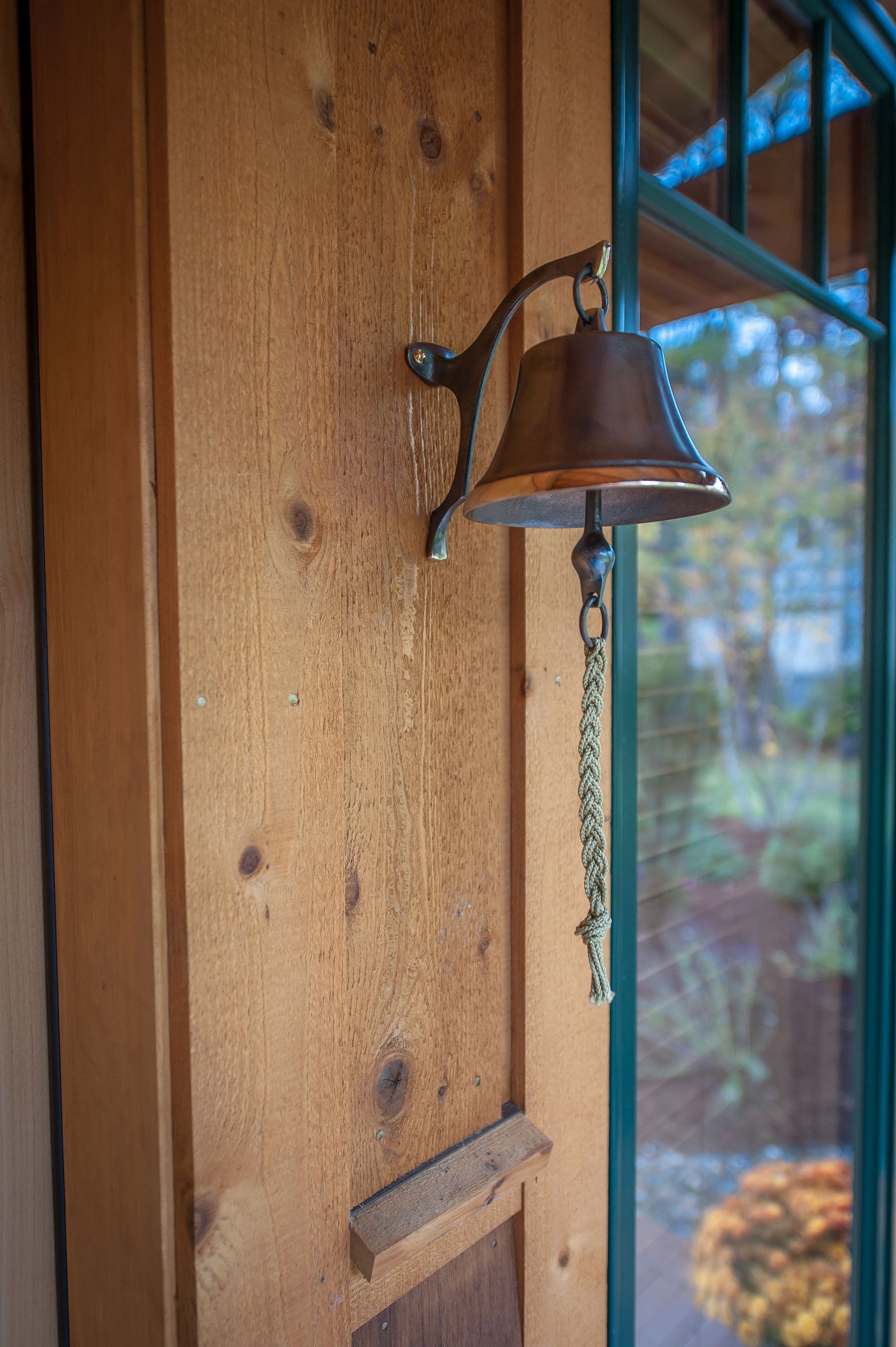 Bronze bell with chain mounted on a wooden wall next to a window.