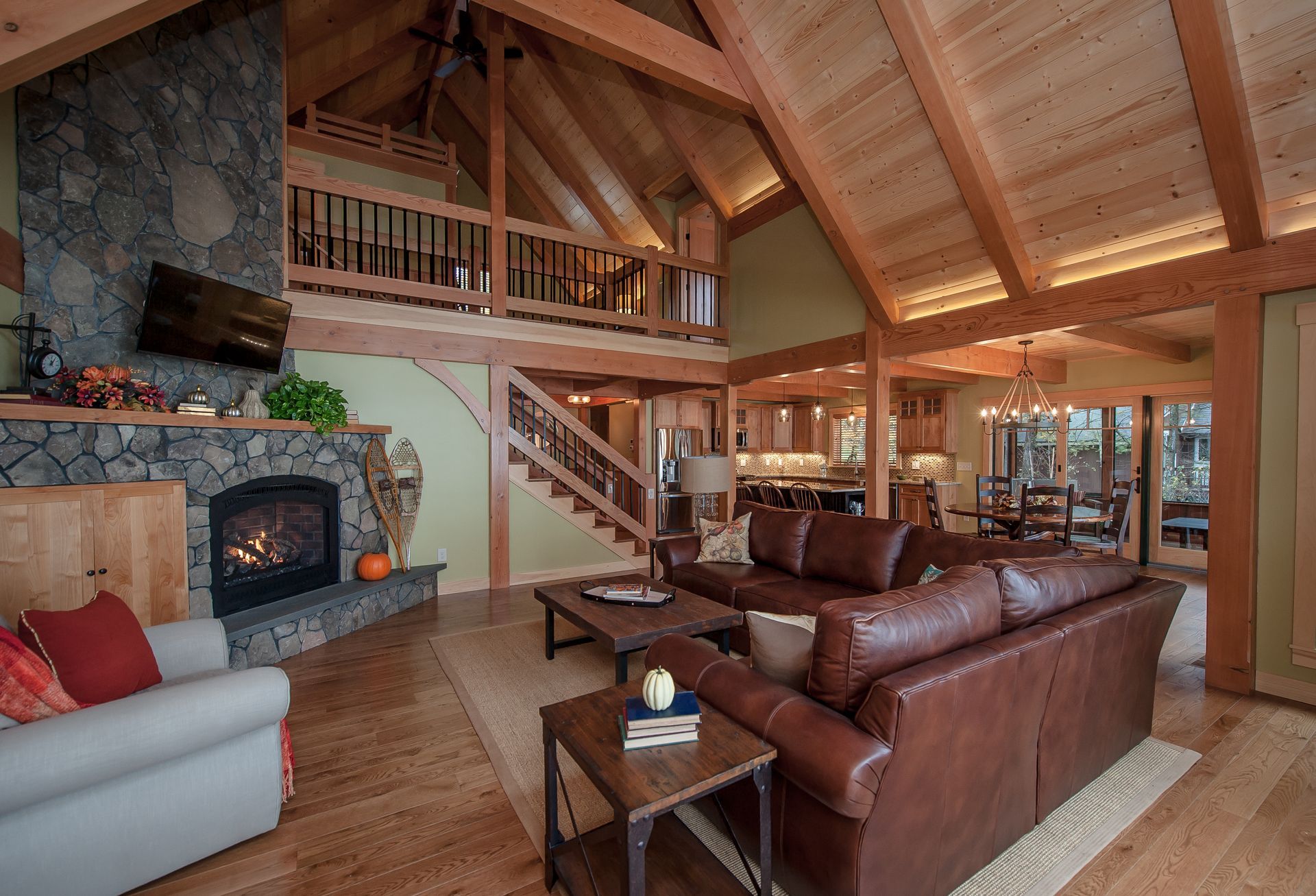 Living room with a stone fireplace, brown leather sofa, wood beams, and a loft.