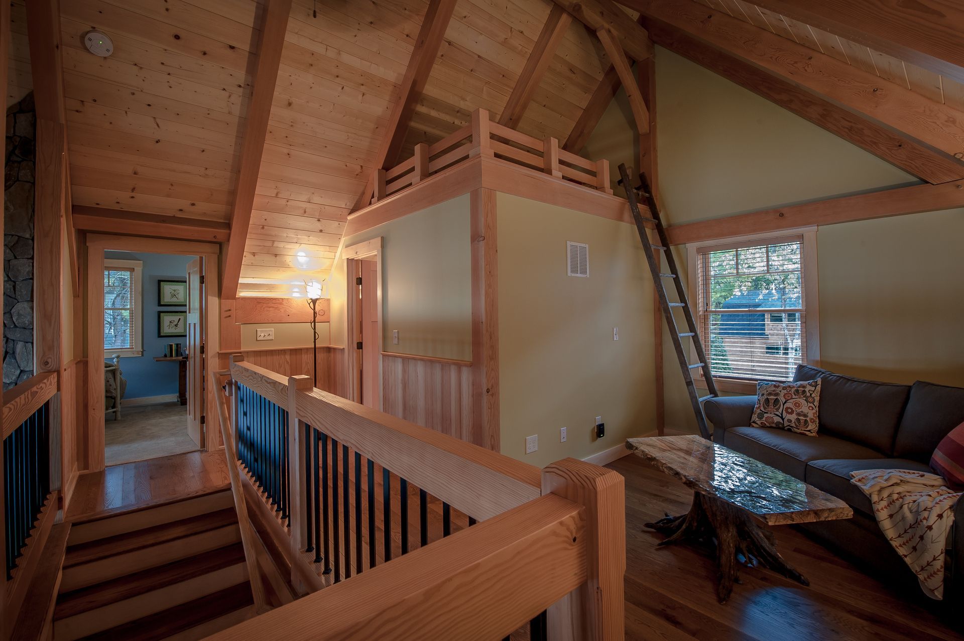 Interior of a cabin loft with wooden beams and a seating area. There's a ladder leading to a small platform.