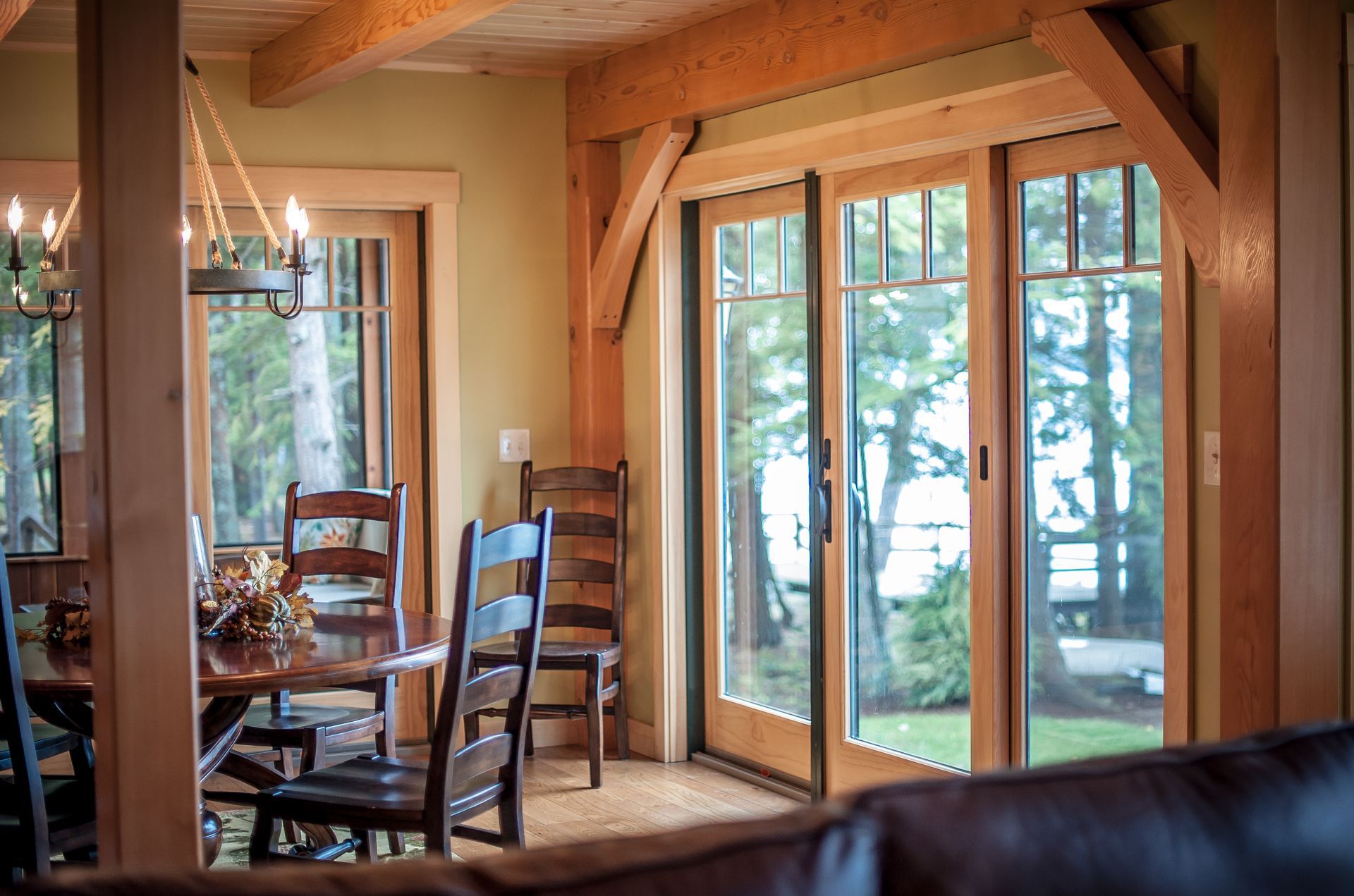 Dining room with wooden table, chairs, and sliding glass doors with a view of trees and water.