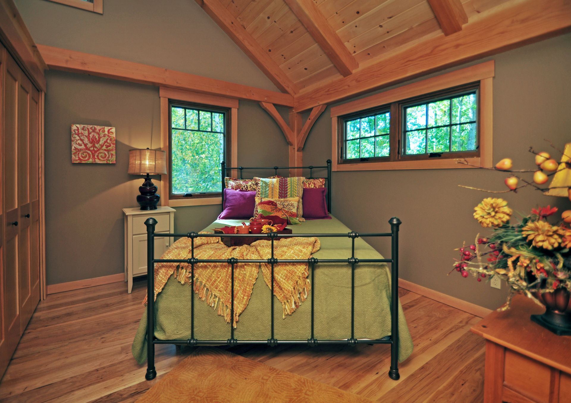 Bedroom with green bed, wooden floor and beams, and two windows.