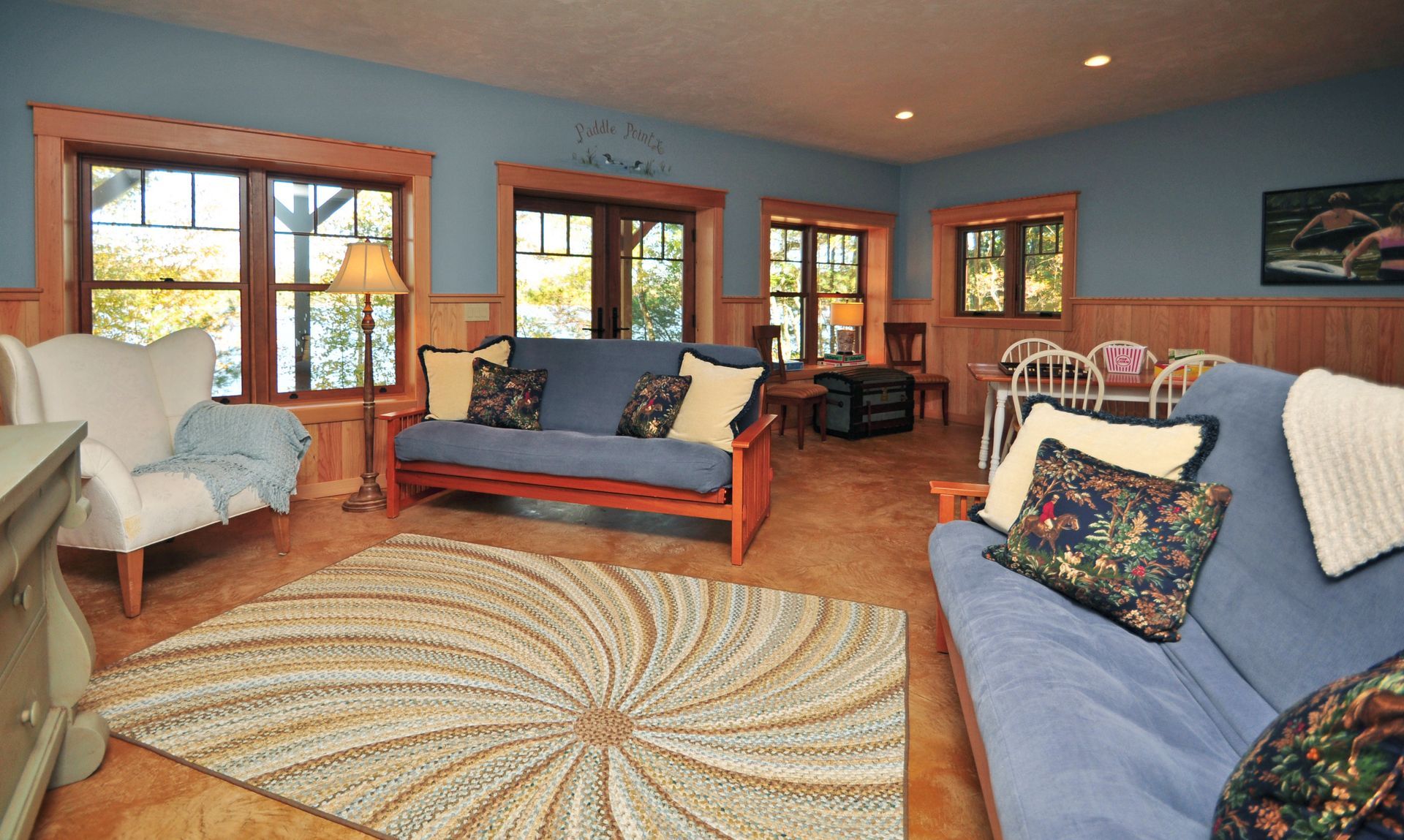 Living room with blue walls, wooden trim, futon sofas, and spiral rug.