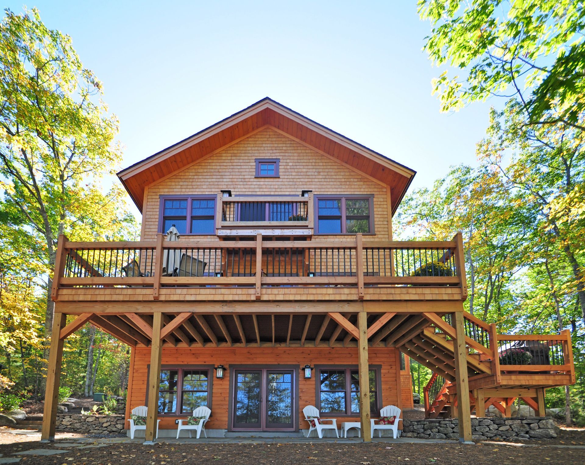 Wooden cabin with large deck, surrounded by trees.