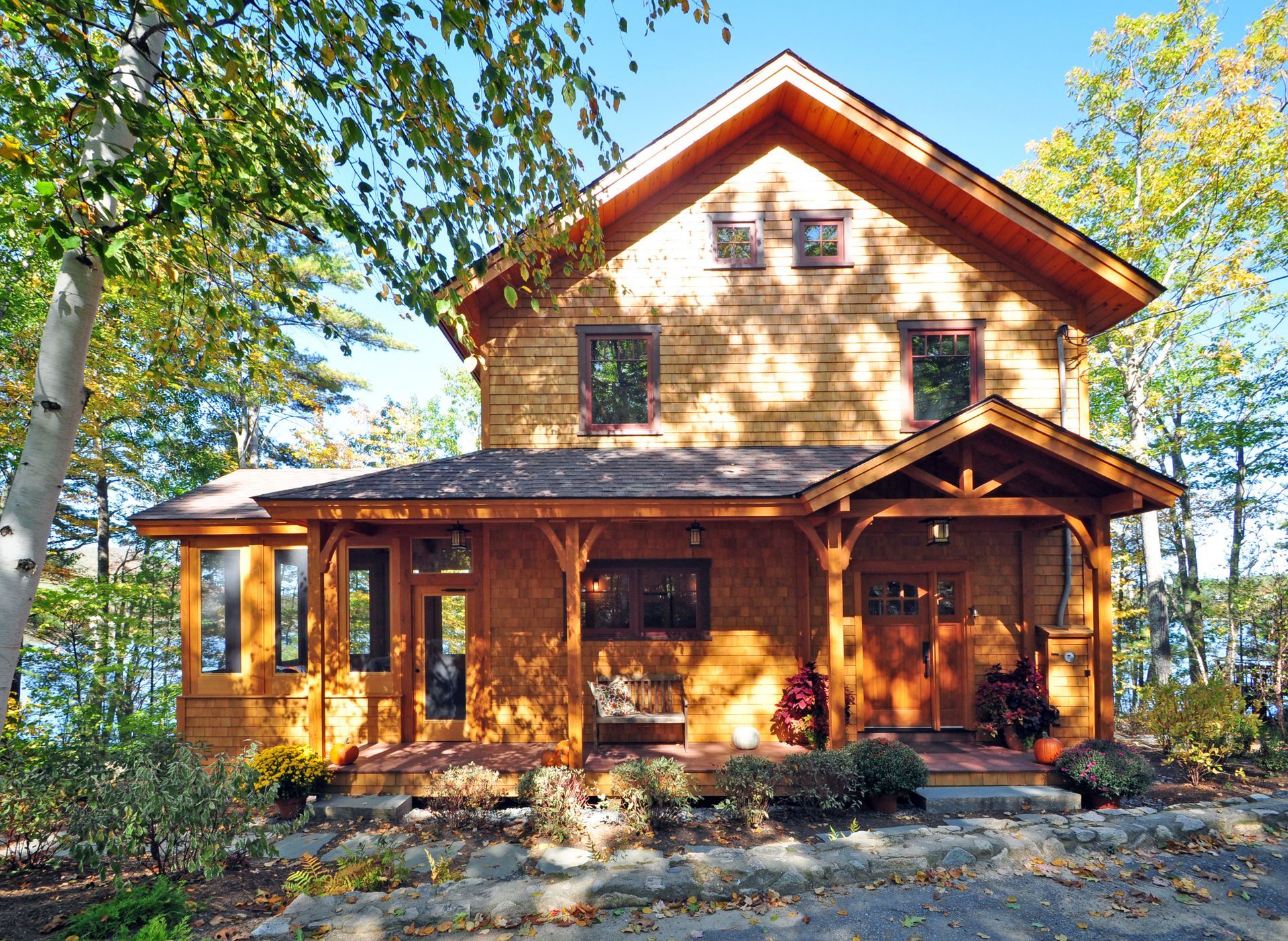 Wooden two-story house with a porch and surrounding trees bathed in sunlight.