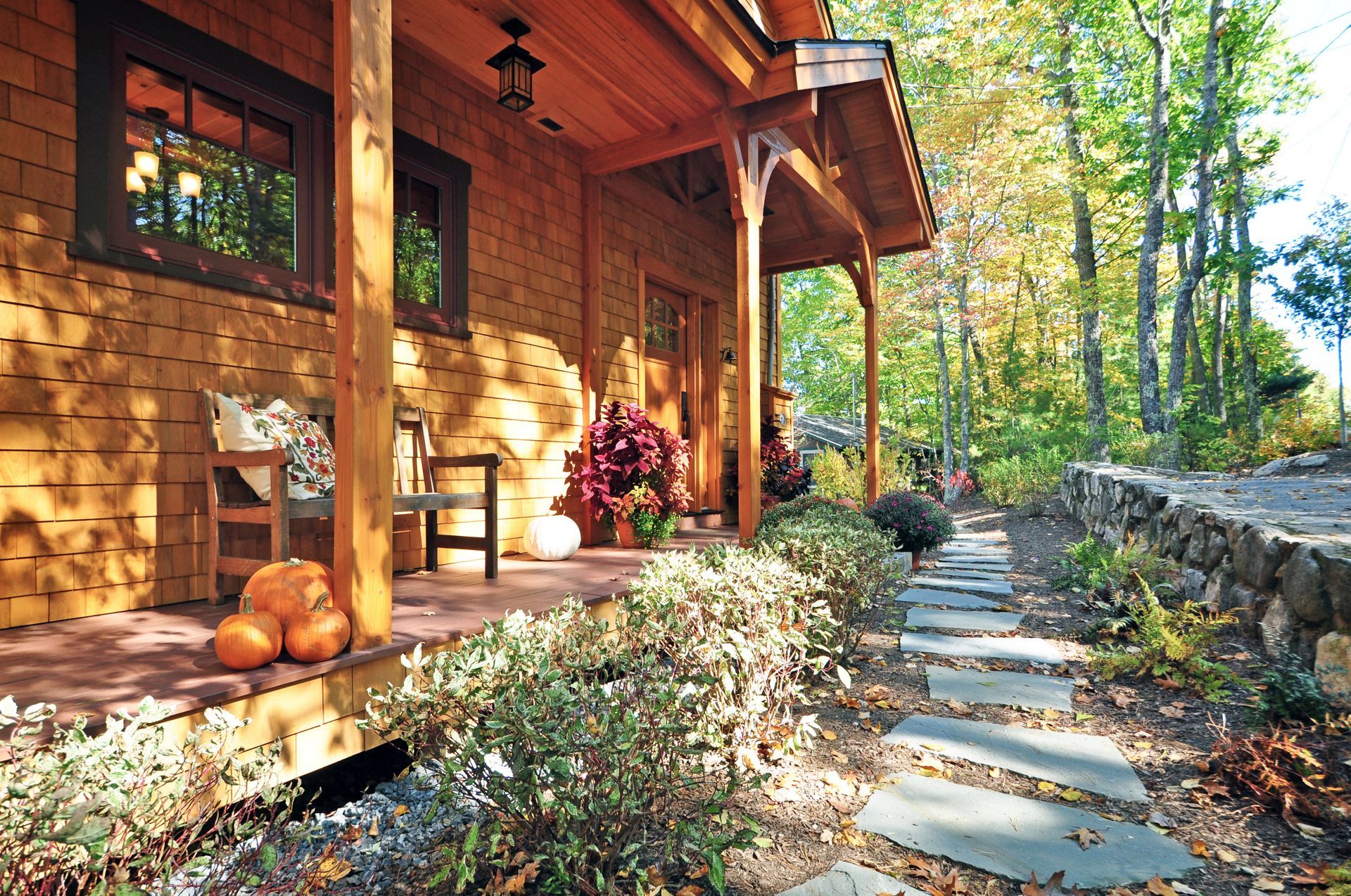 Wooden porch with pumpkins, plants, and stone path leading into trees.