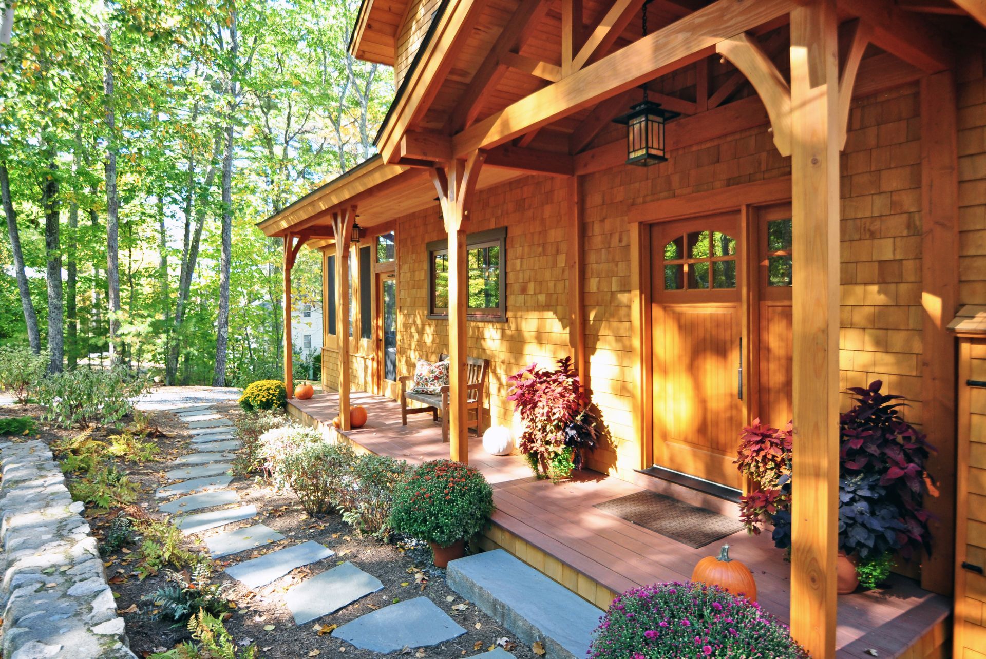 Wooden cabin with a porch, front door, and walkway; surrounded by trees and colorful plants.