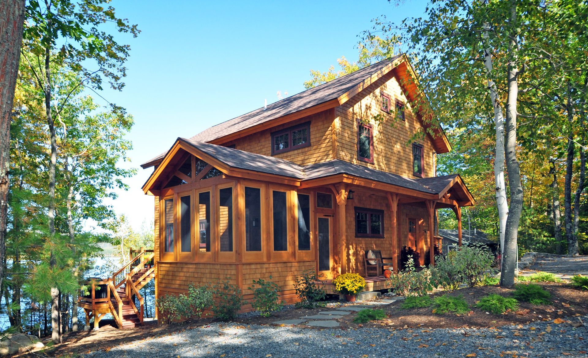 Wooden cabin with porch and screened-in sunroom surrounded by trees under a blue sky.