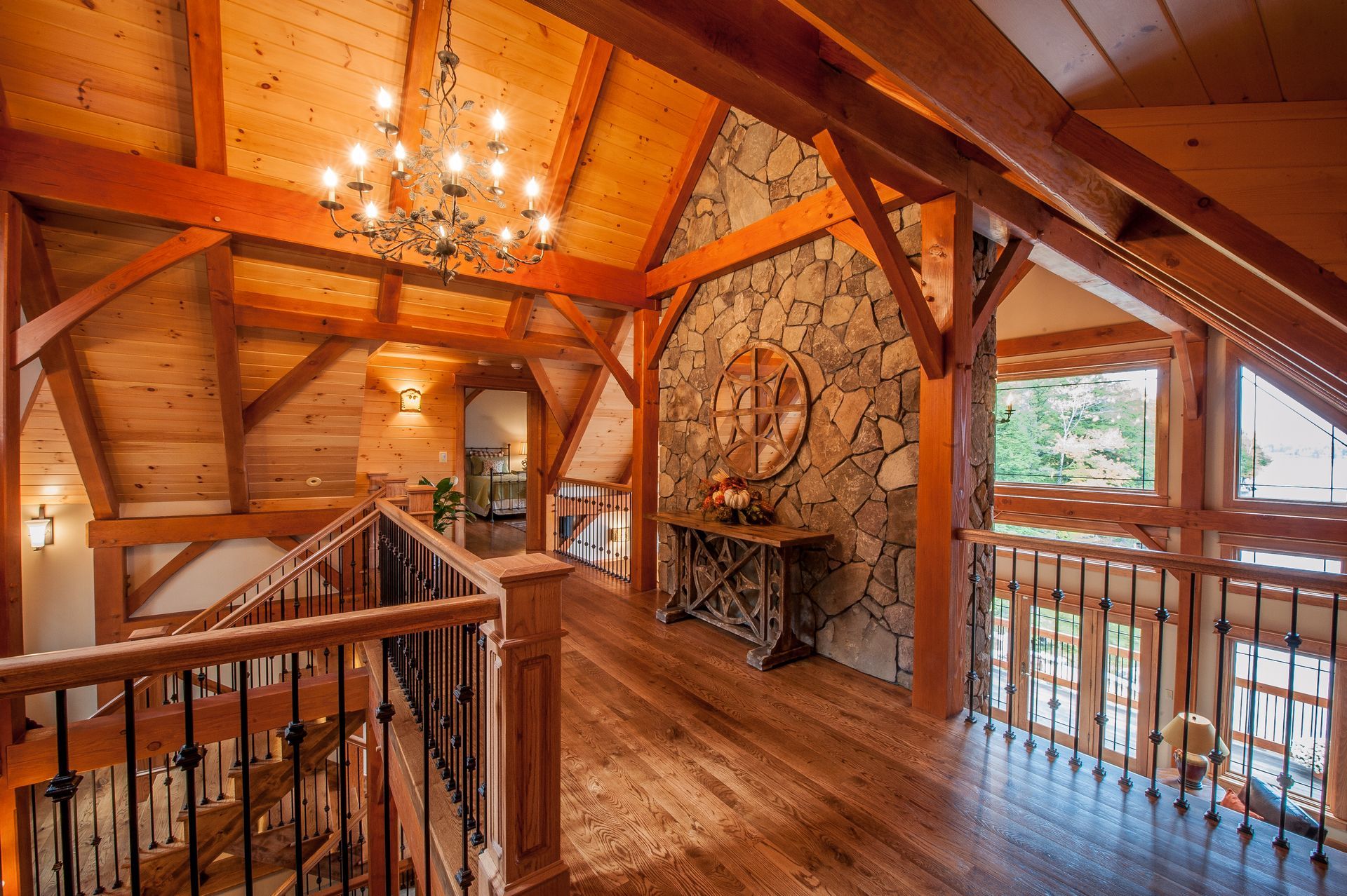 Interior shot of a wood-beamed hallway with a stone accent wall, chandelier, and staircase with iron railings.
