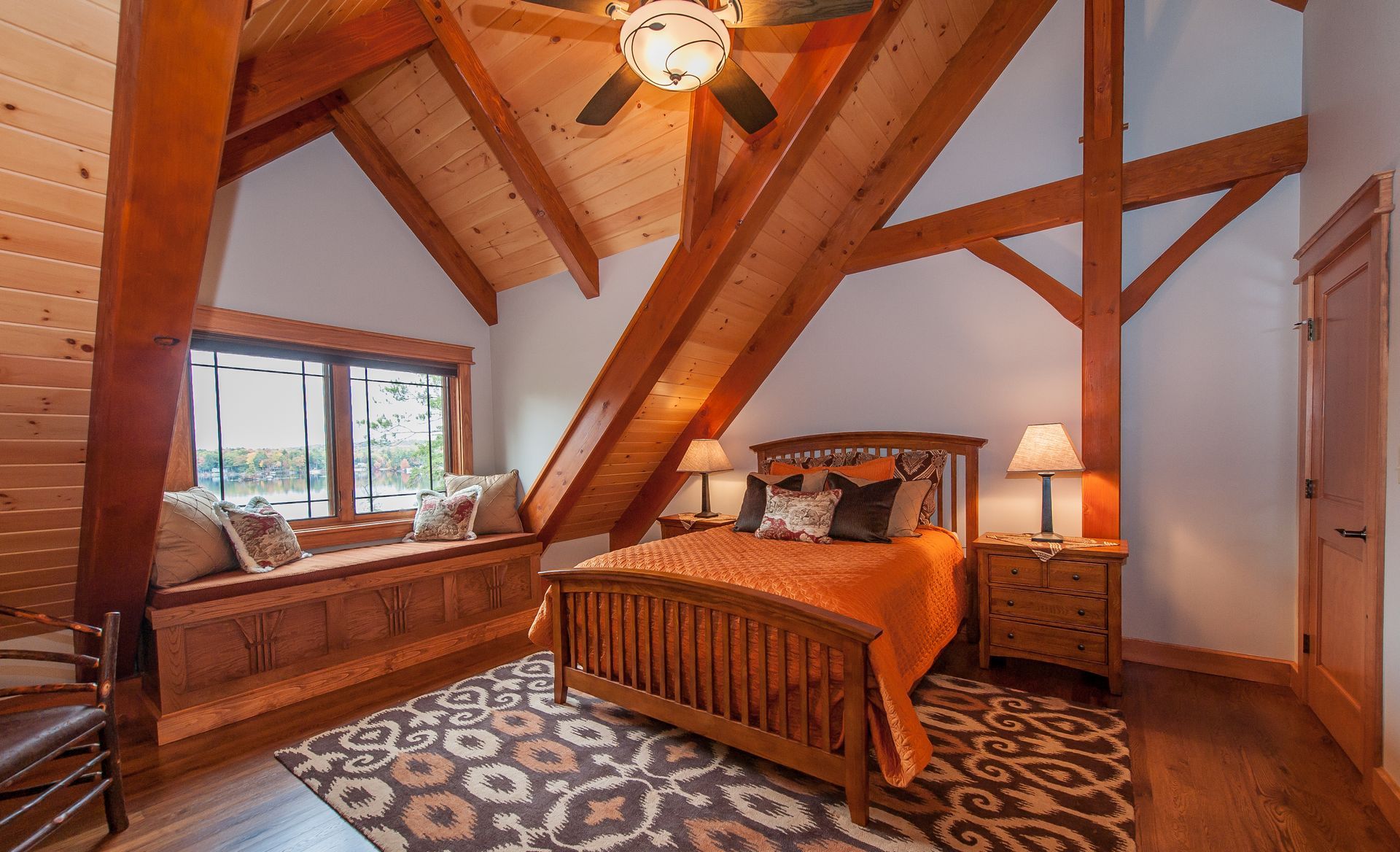 Bedroom with wooden bed, window seat, exposed beams, and patterned rug.