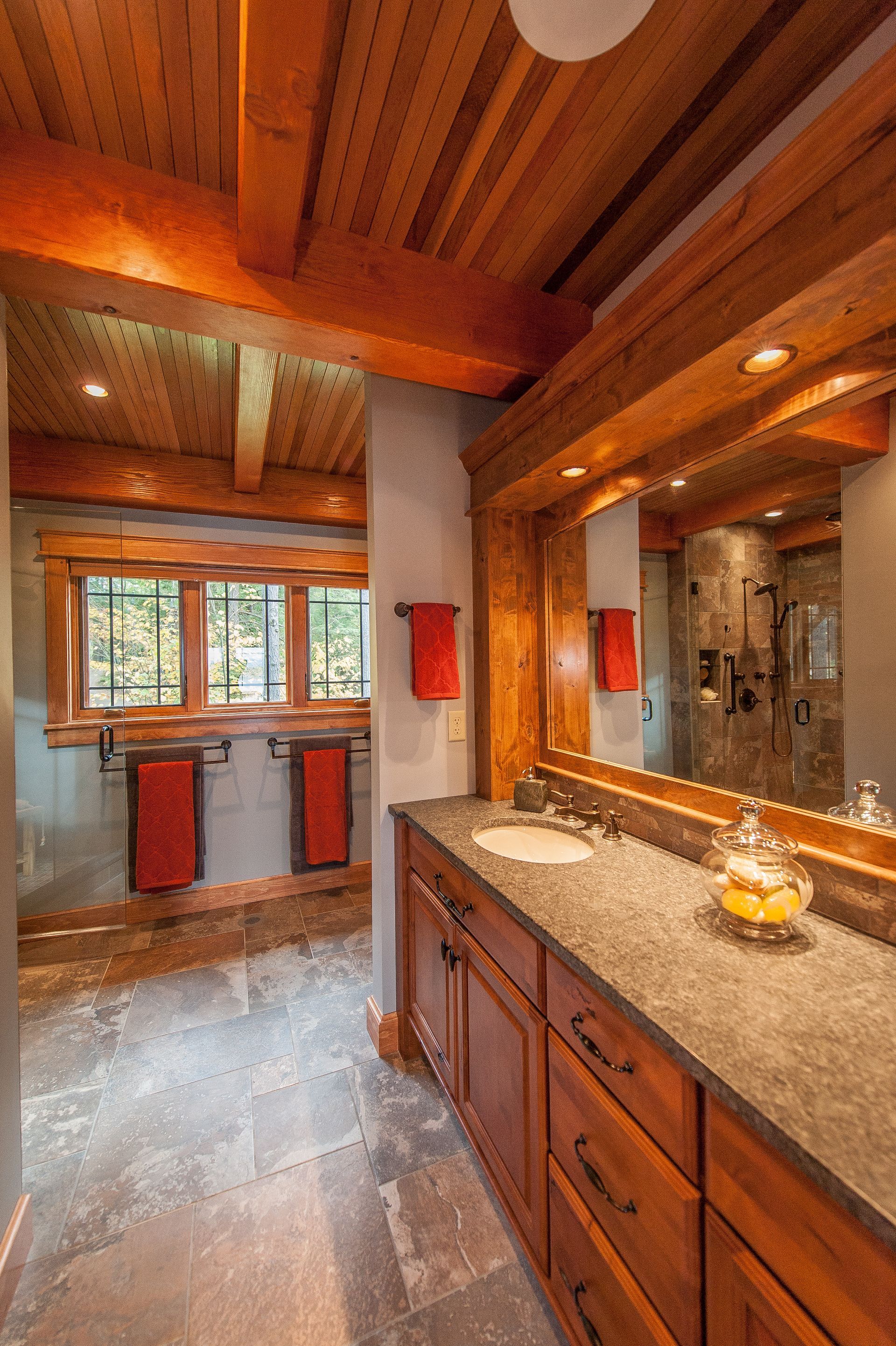Bathroom with wood beams, cabinetry, stone countertop, and two red hand towels.