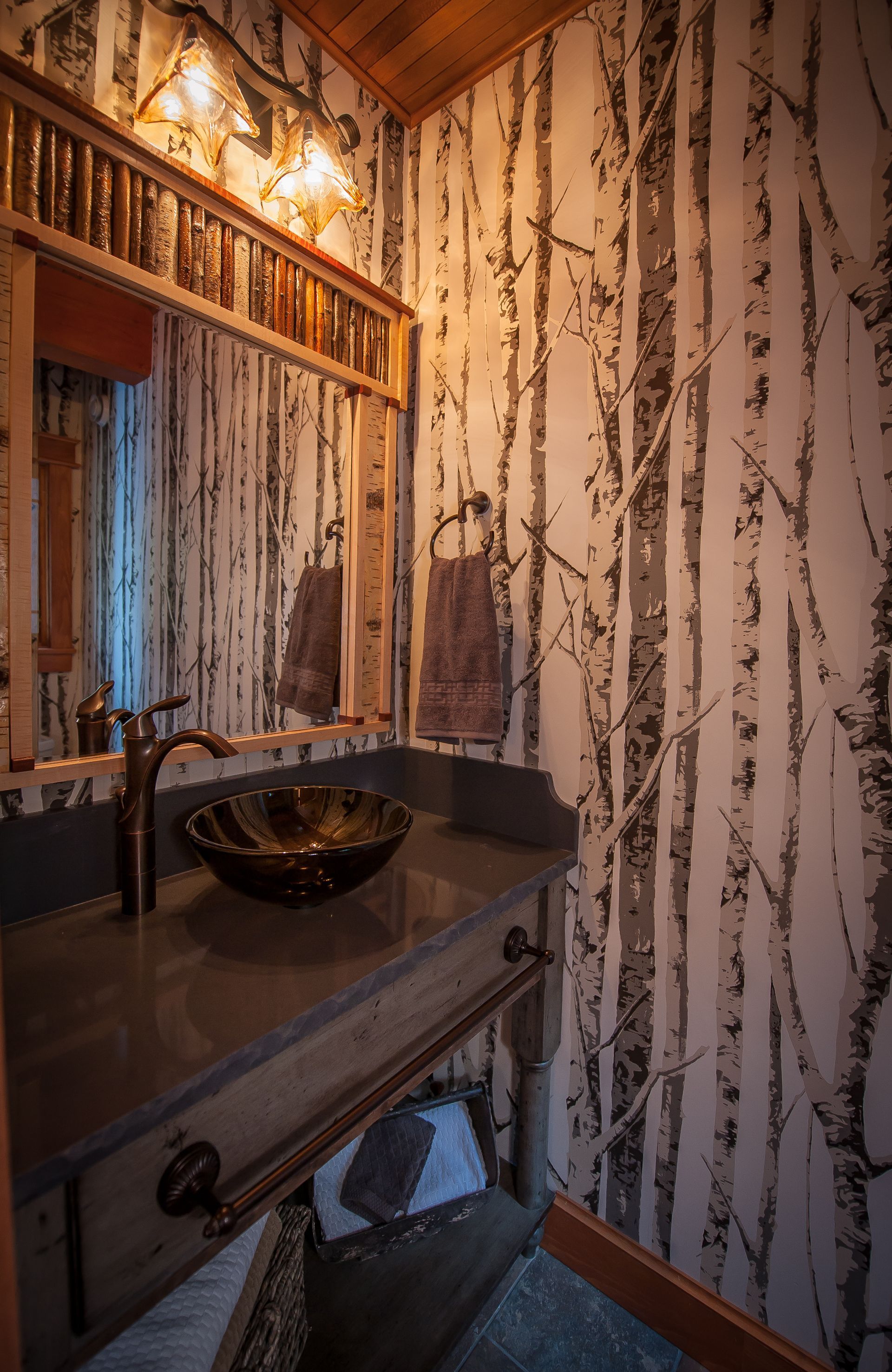 Rustic bathroom with birch tree wallpaper, dark sink, and copper fixtures.