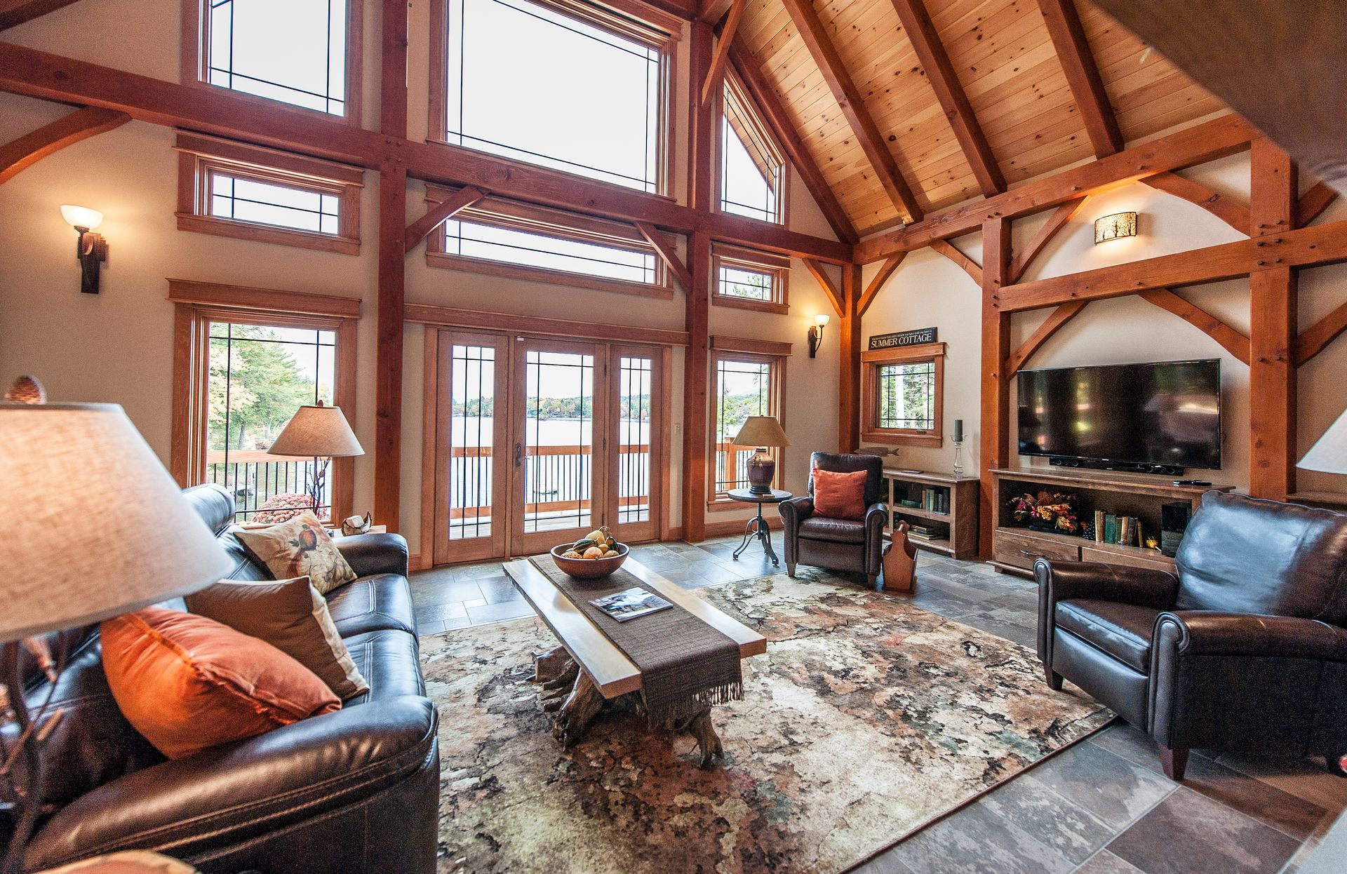 Living room with wood beams, high windows, leather furniture, and a rug.