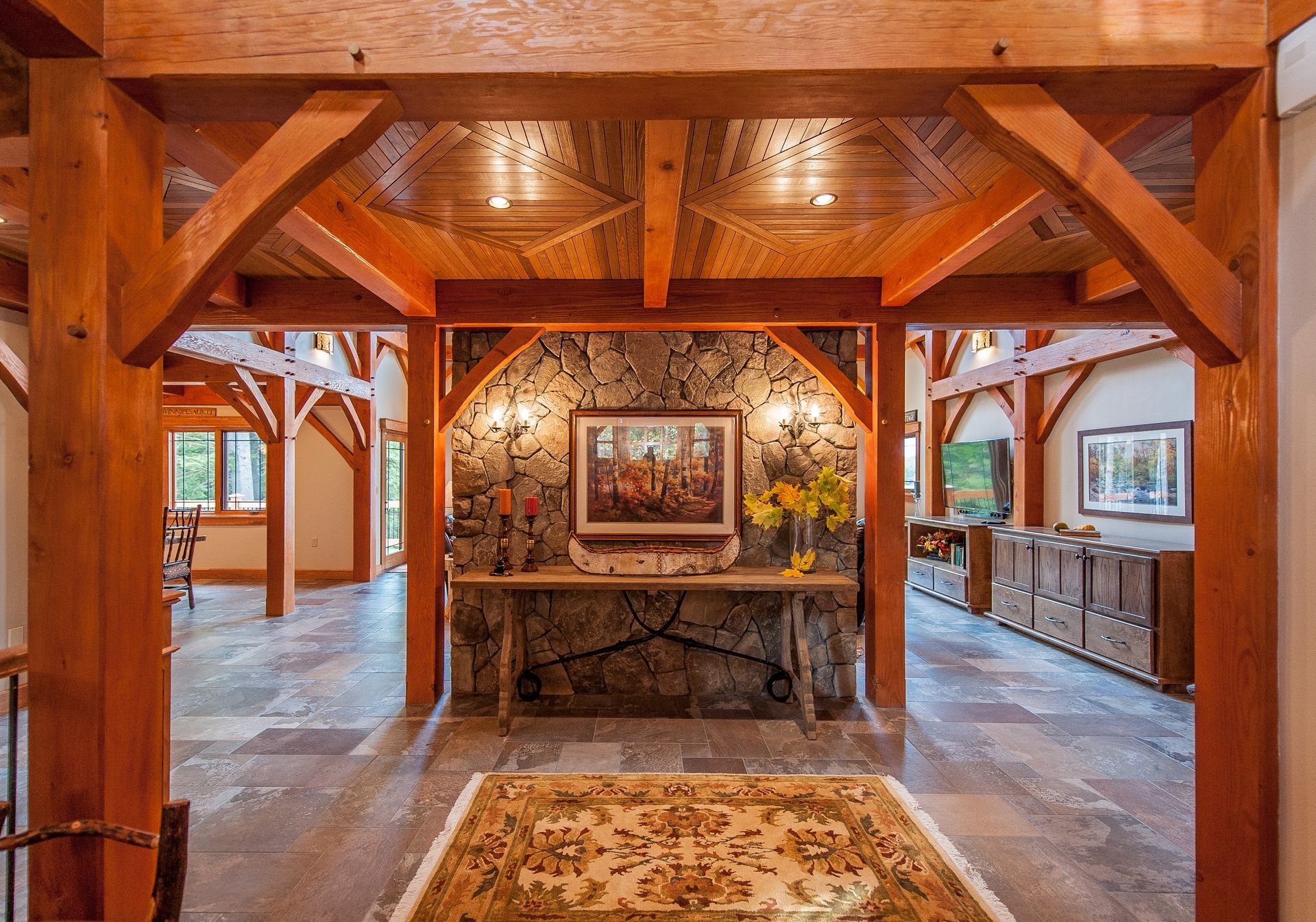 Wooden beam archway frames a stone wall with a painting and console table. Interior with stone floor and rug.
