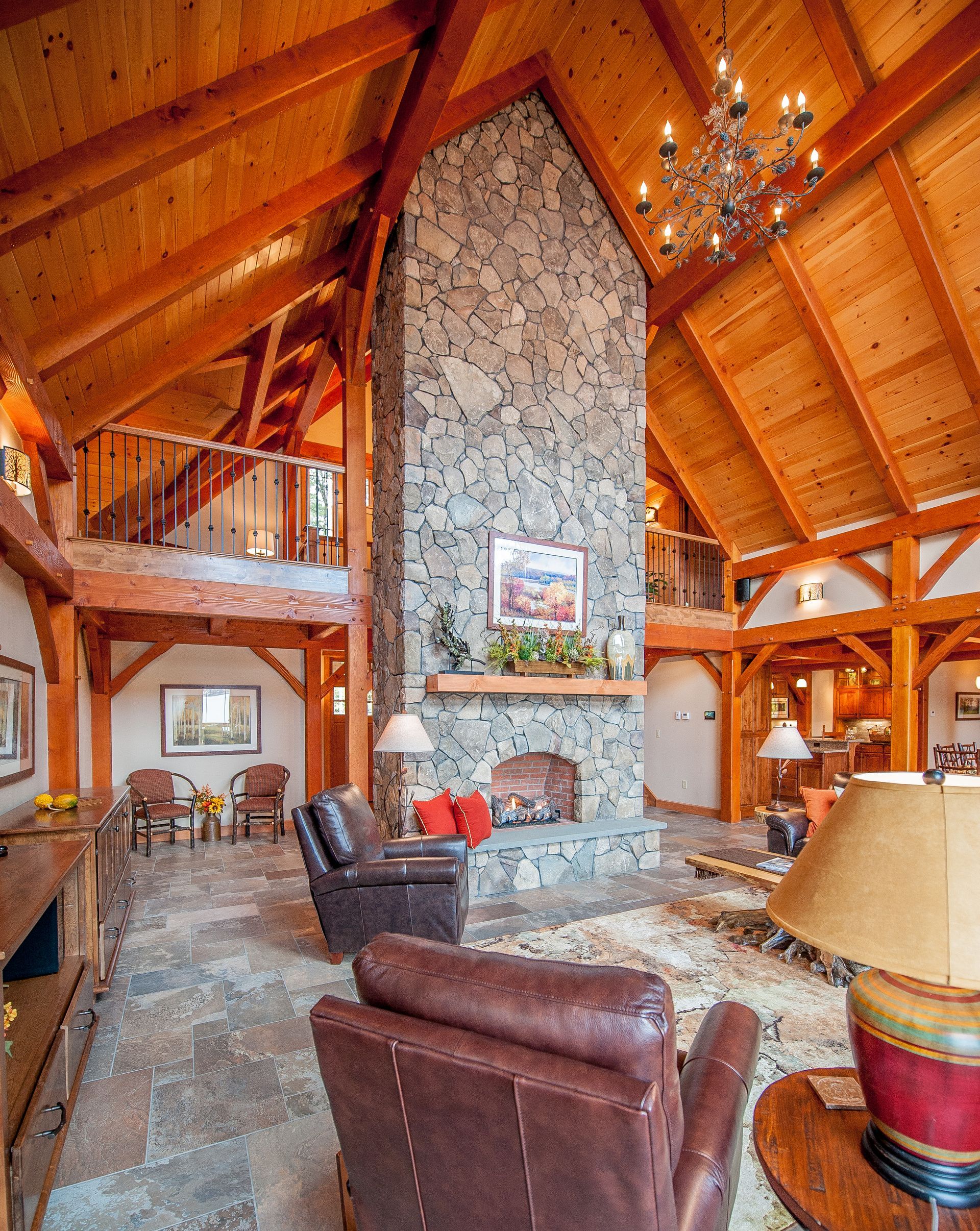 Stone fireplace in a timber-framed living room with leather chairs and a mezzanine.