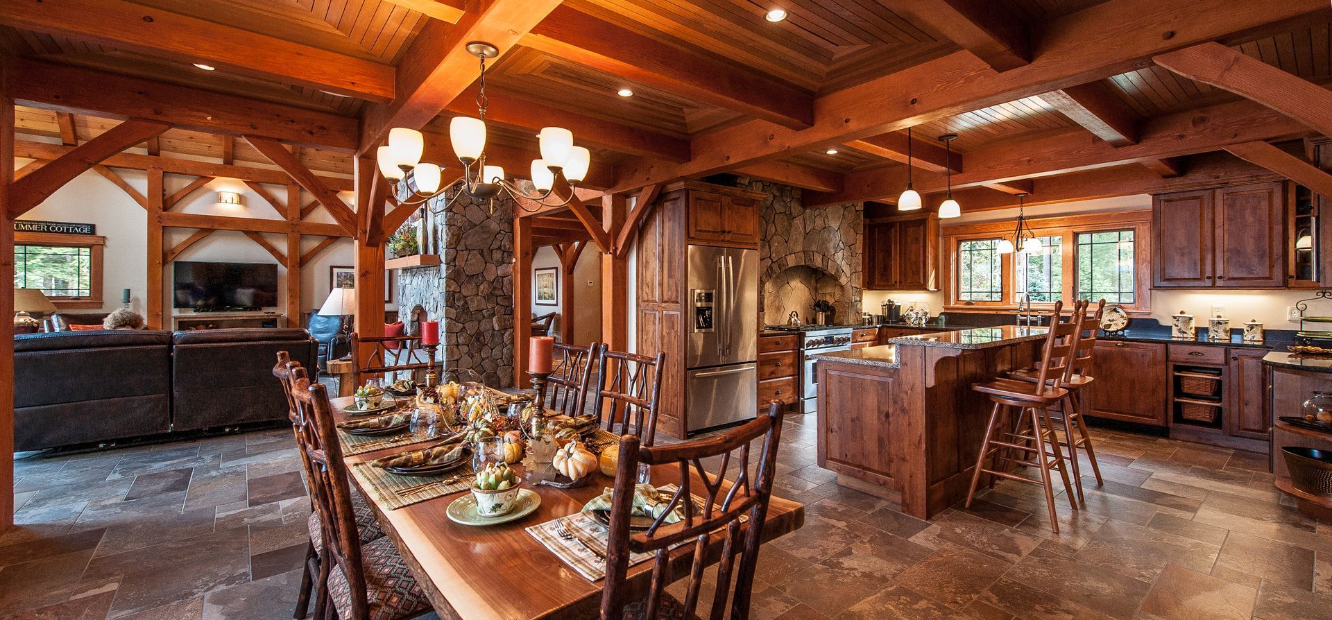 Rustic open-concept kitchen and dining area with exposed wood beams, stone accents, and a long dining table.