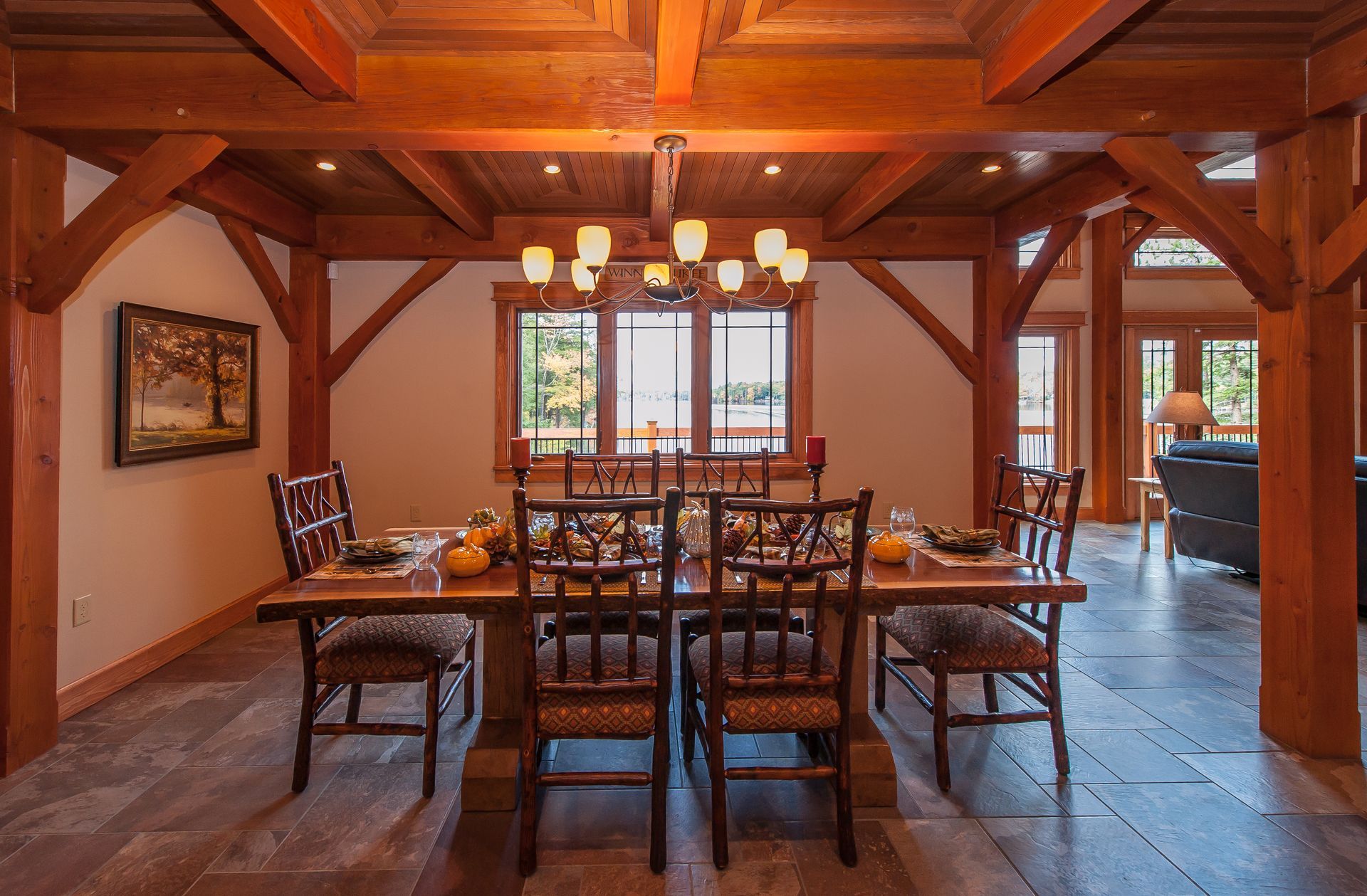 Dining room with a wooden table and chairs, set for a meal. Exposed wood beams and a chandelier are overhead.