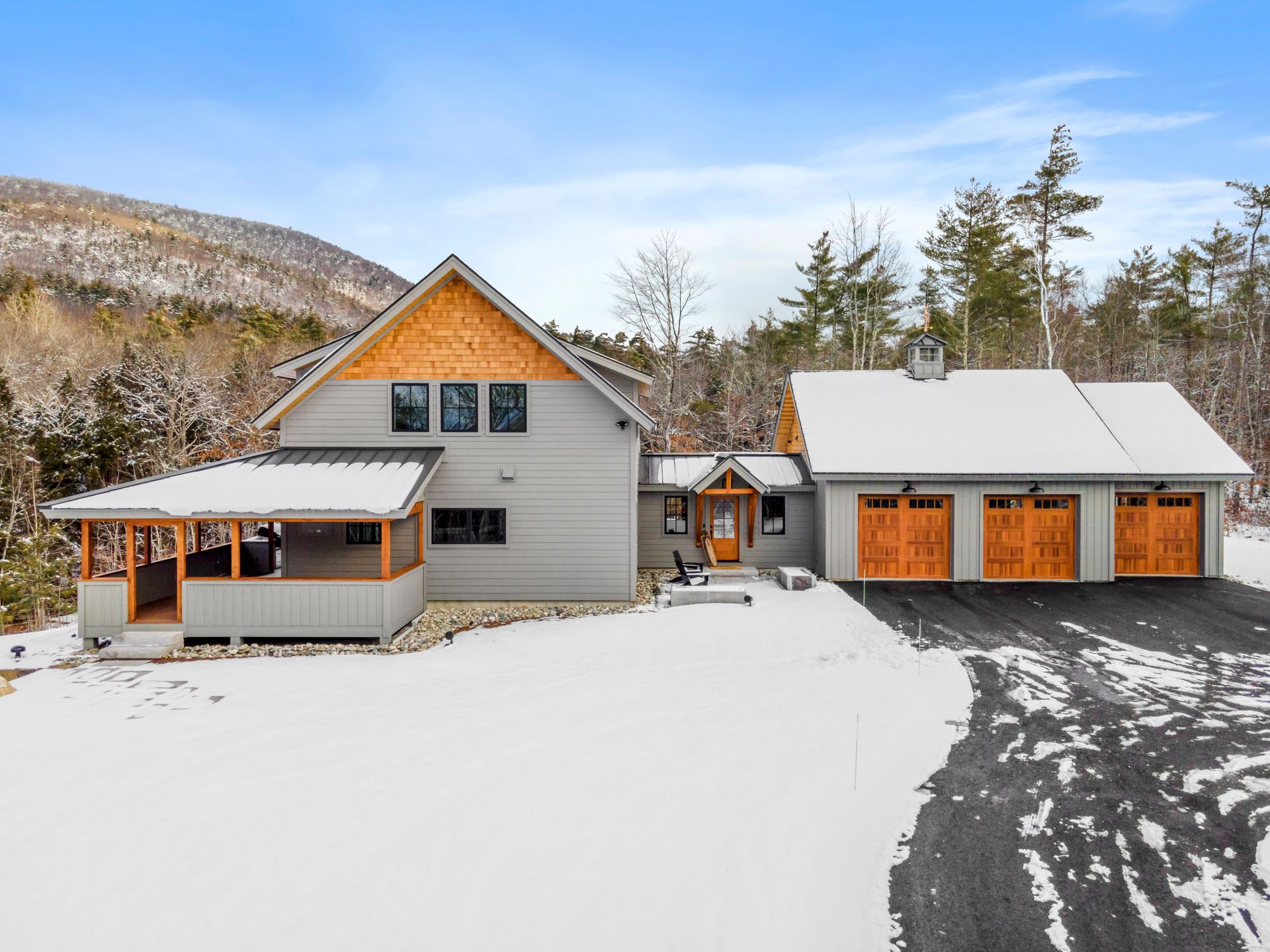 House with a porch and garage, covered in snow, with a mountain backdrop.