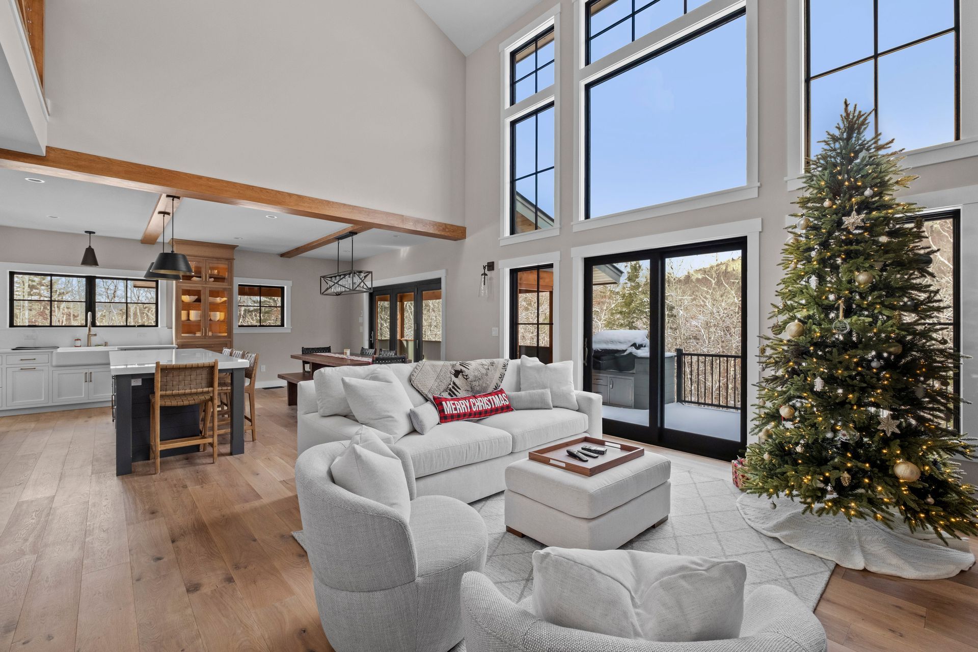 Spacious living room with Christmas tree, large windows, and white sofa, wooden beams, and hardwood floors.