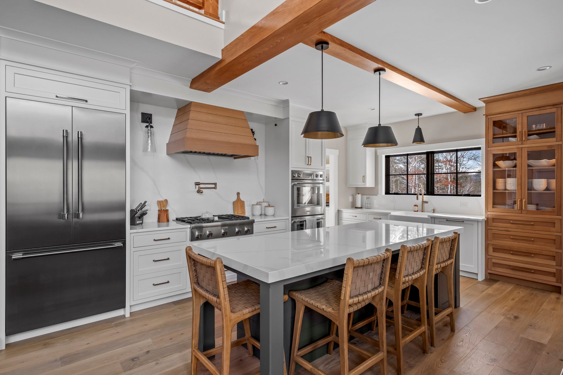 Modern kitchen with large island, stainless steel appliances, wood accents, and pendant lights.
