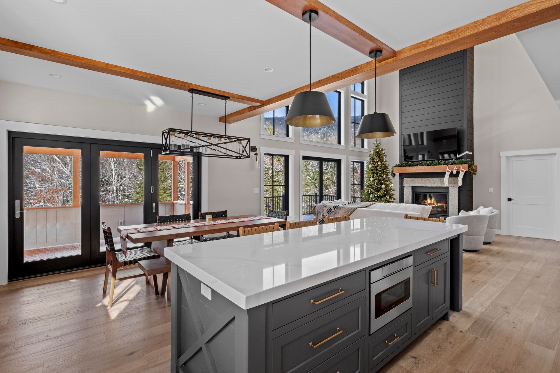 Modern kitchen with island, dining area, and fireplace. Gray and white interior with wood accents and natural light.