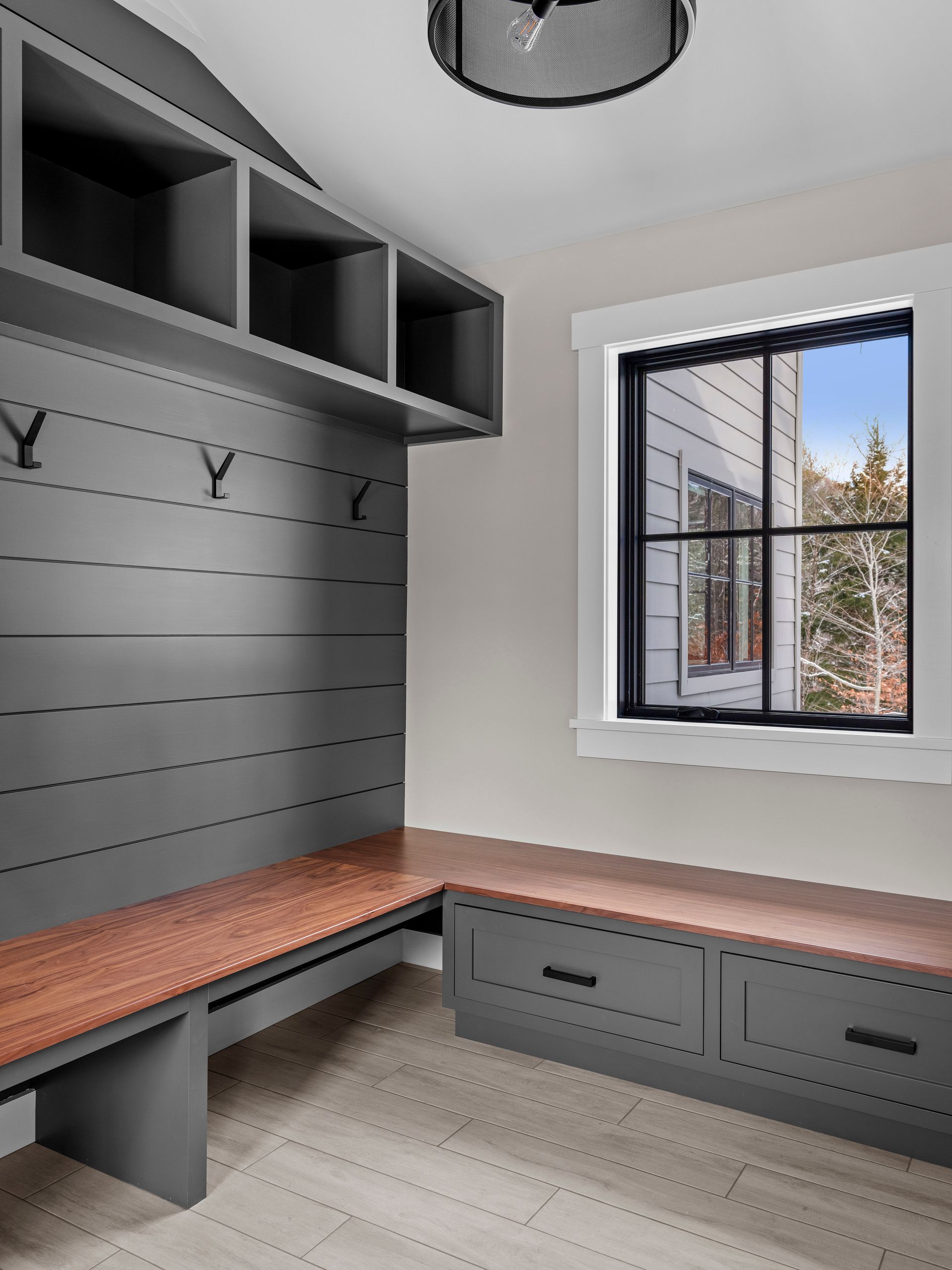 Gray and wood mudroom with bench seating, window, and overhead storage.