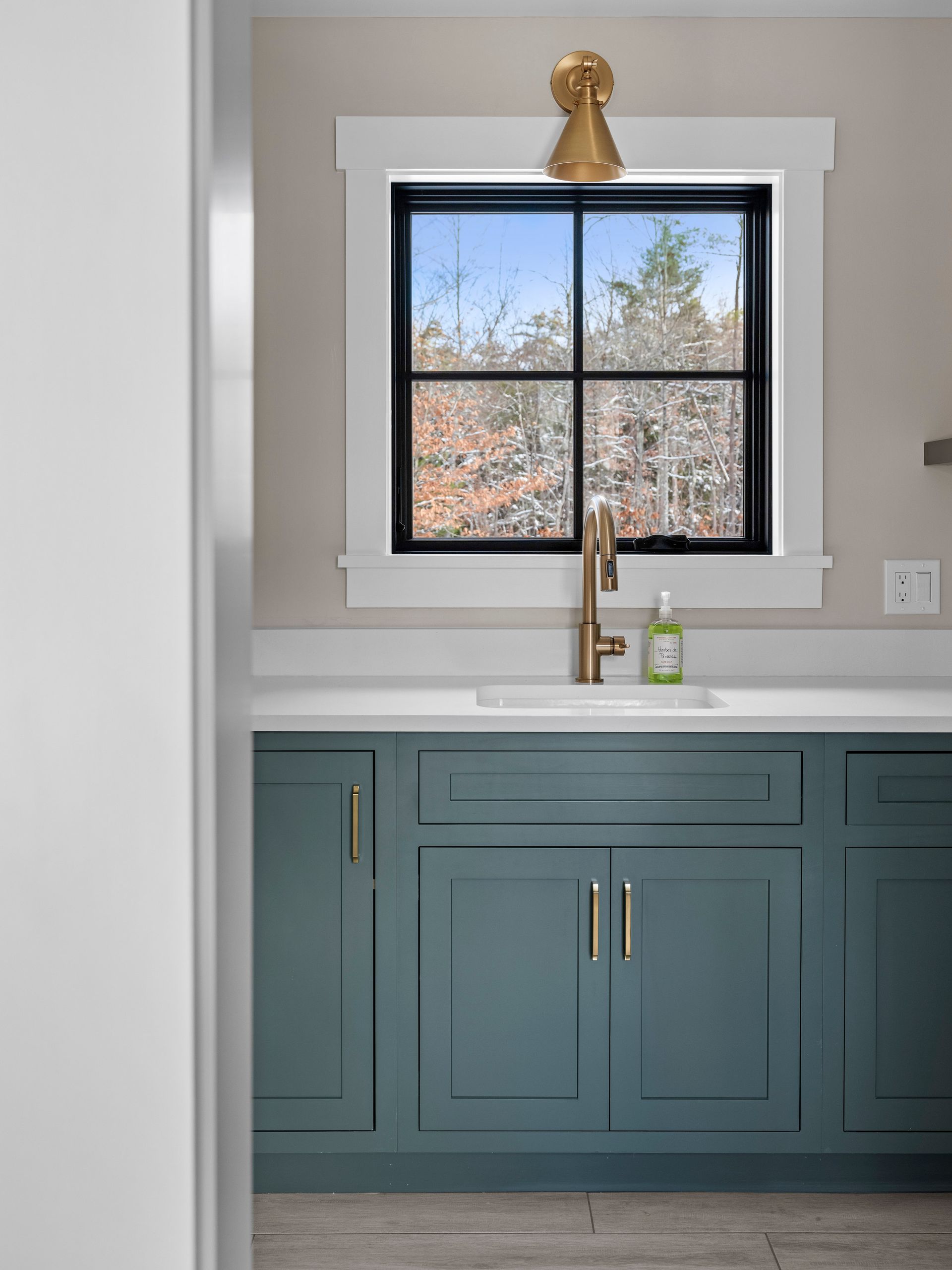 Blue cabinet with a white countertop and gold faucet under a window with a black frame.