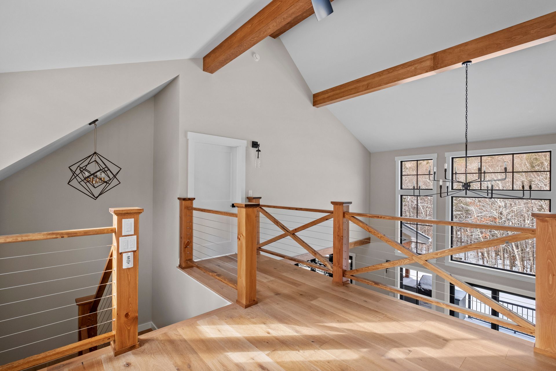 Wooden bridge-style railing on a second-floor hallway, with light wood floor and exposed beams.