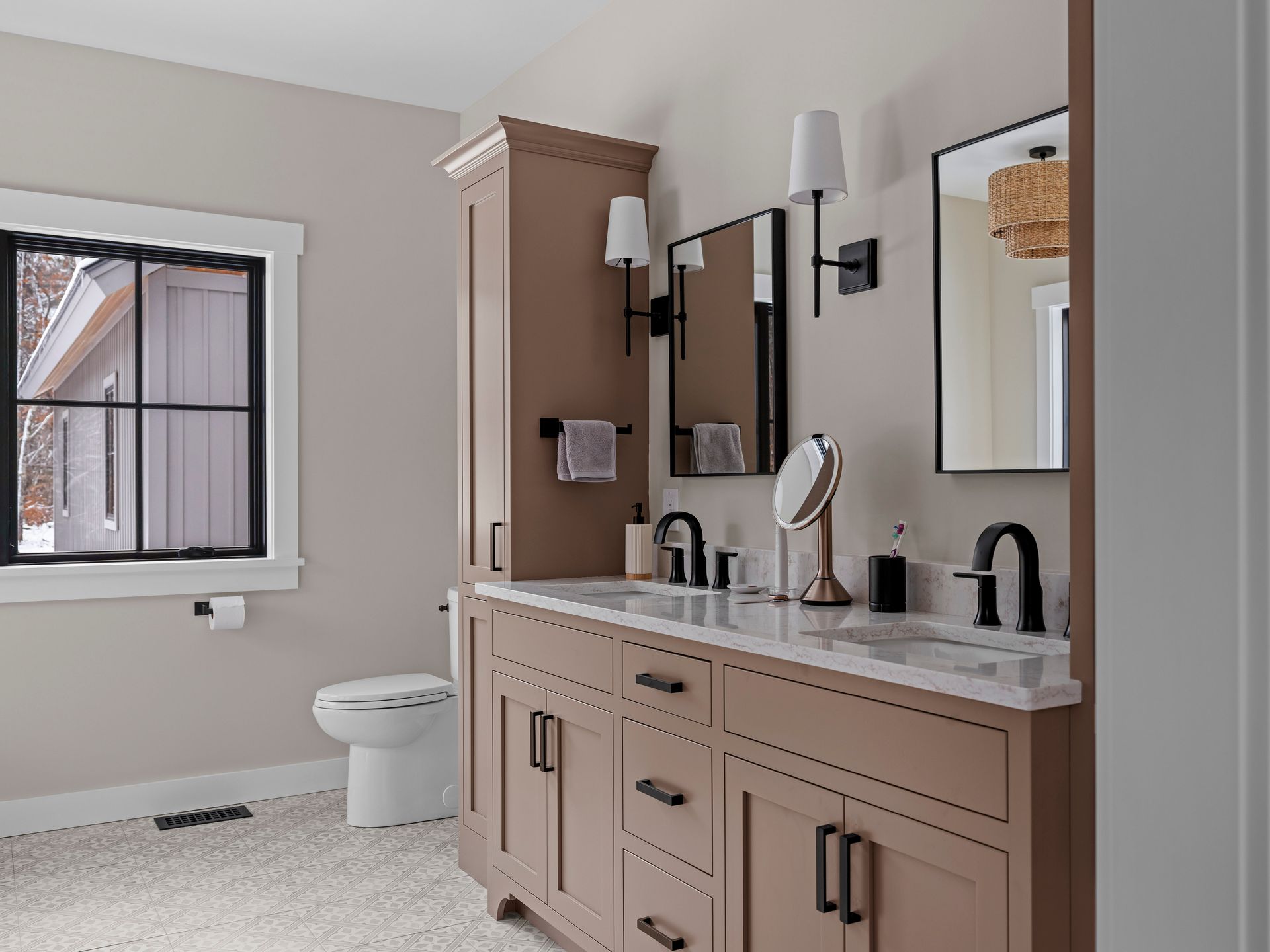 A modern bathroom with a double vanity, tall storage cabinet, and black fixtures.