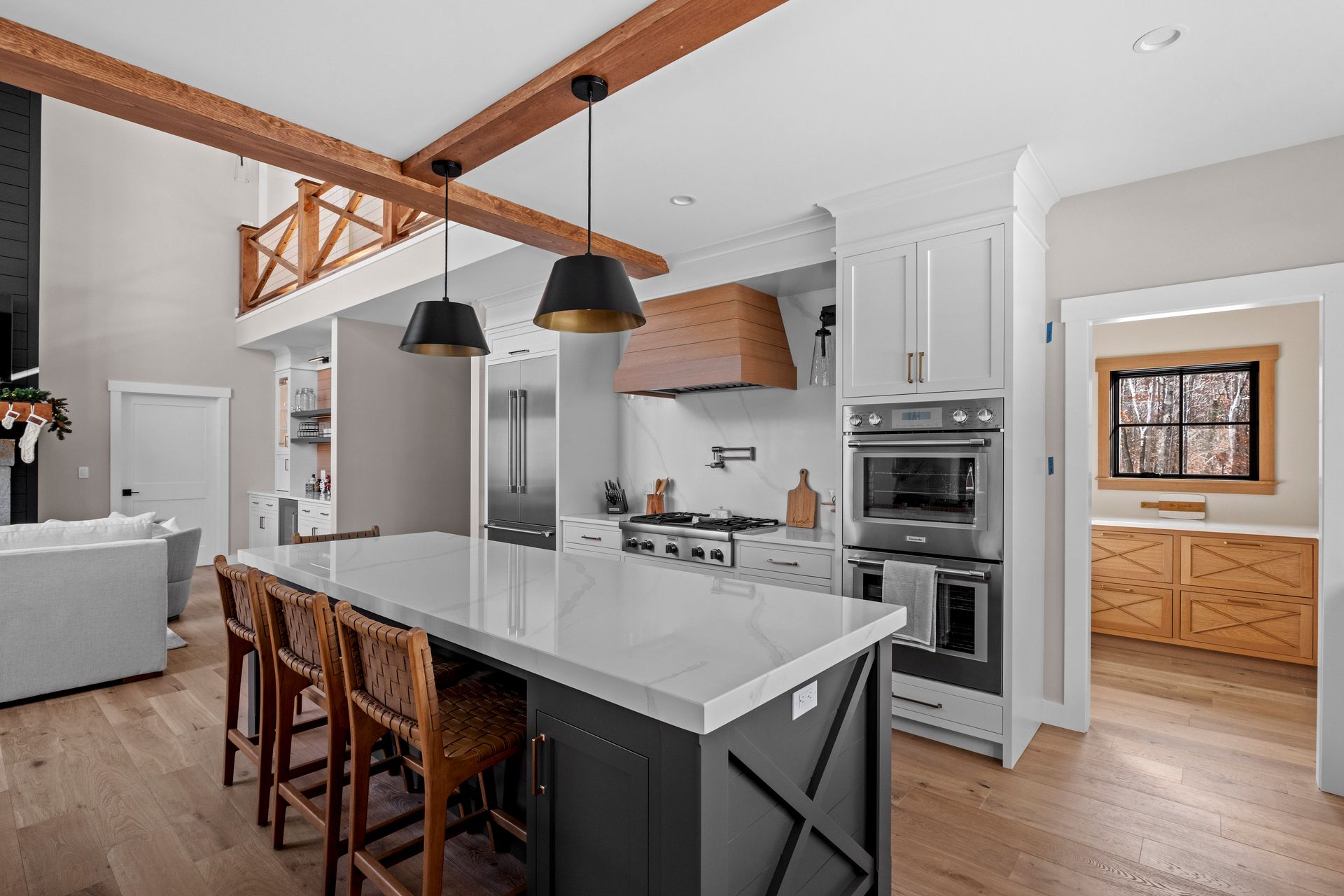 Open-concept kitchen with white cabinets, large island, and wood accents; a second-floor balcony is visible.